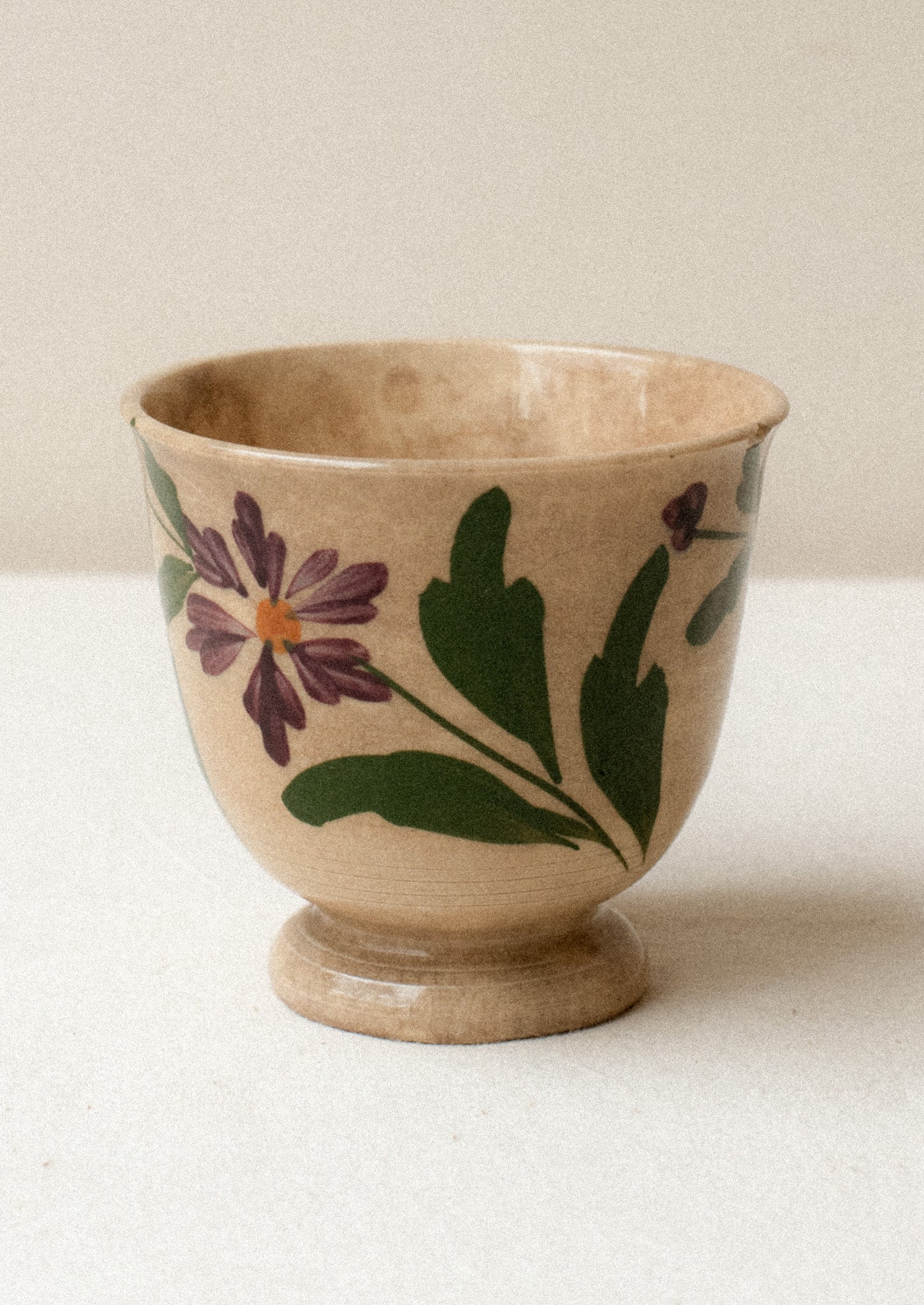A tan ceramic antique tea cup with purple floral pattern.