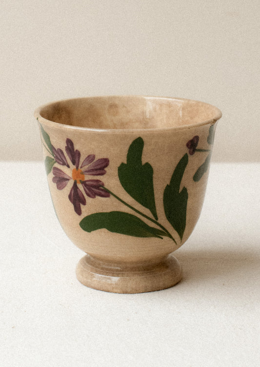 A tan ceramic antique tea cup with purple floral pattern.