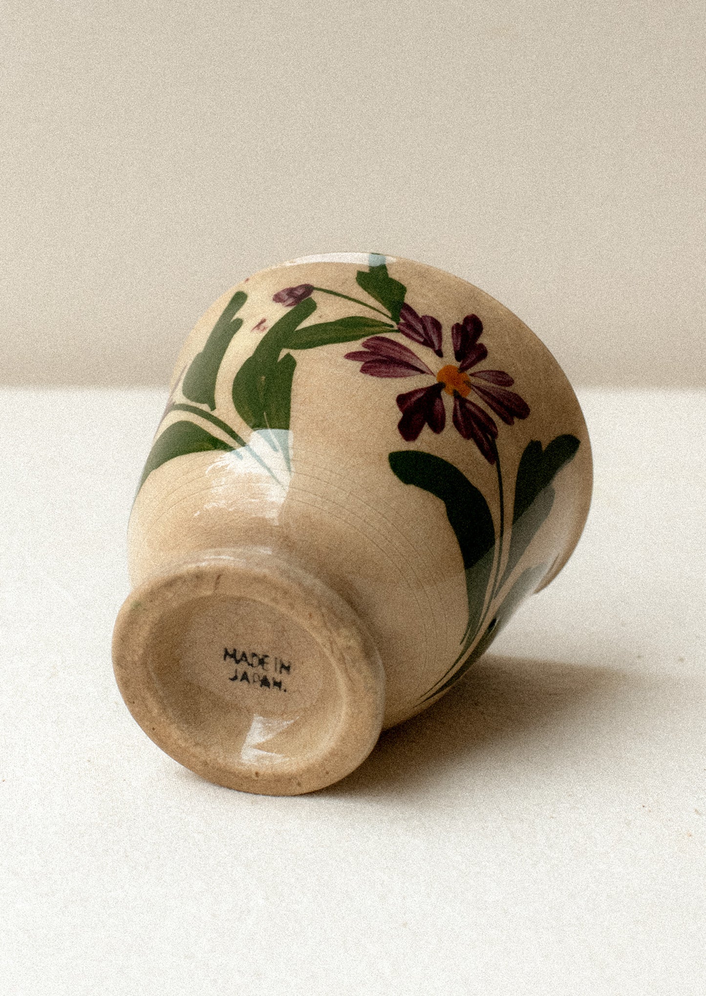 A tan ceramic antique tea cup with purple floral pattern.