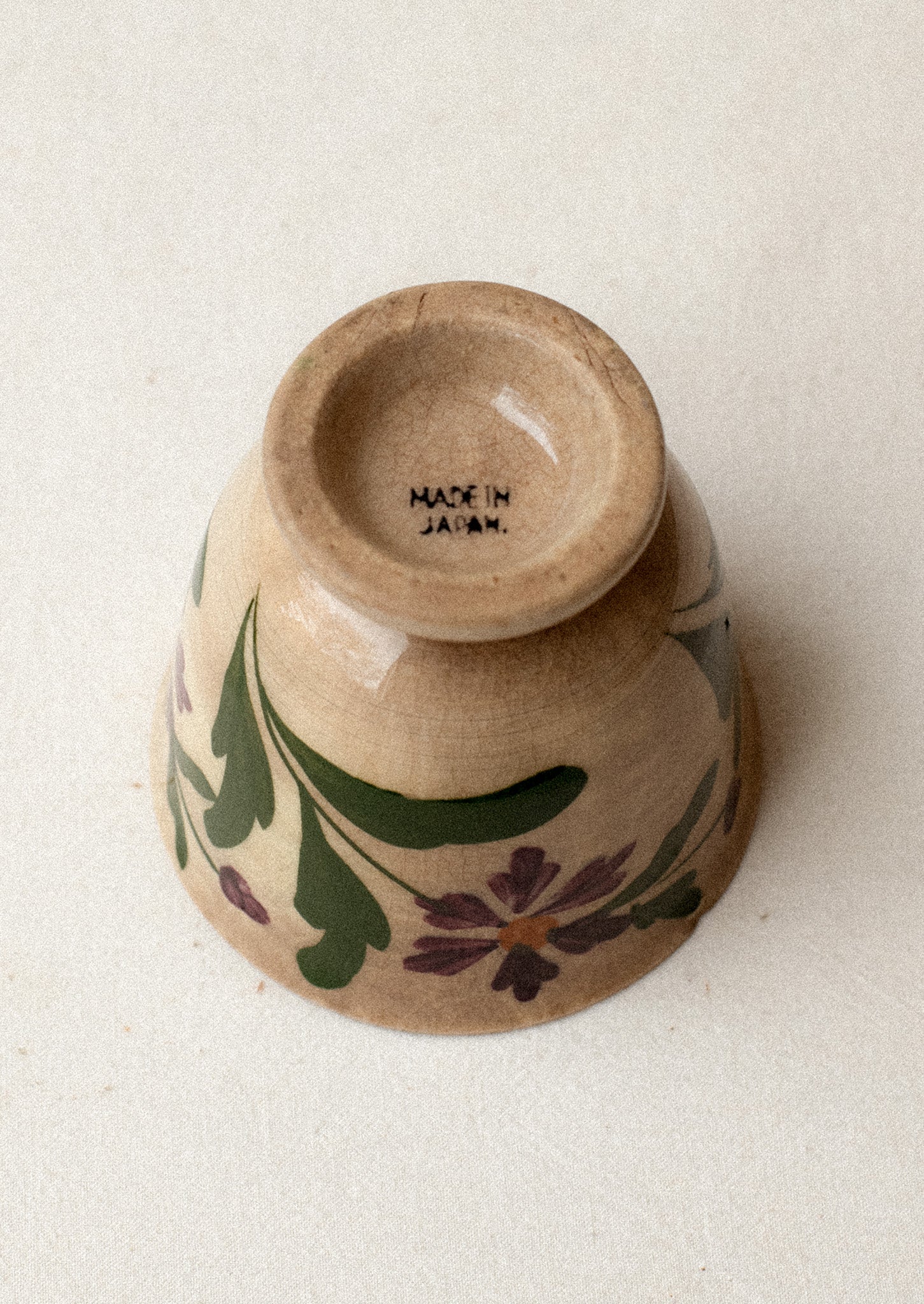 A tan ceramic antique tea cup with purple floral pattern.