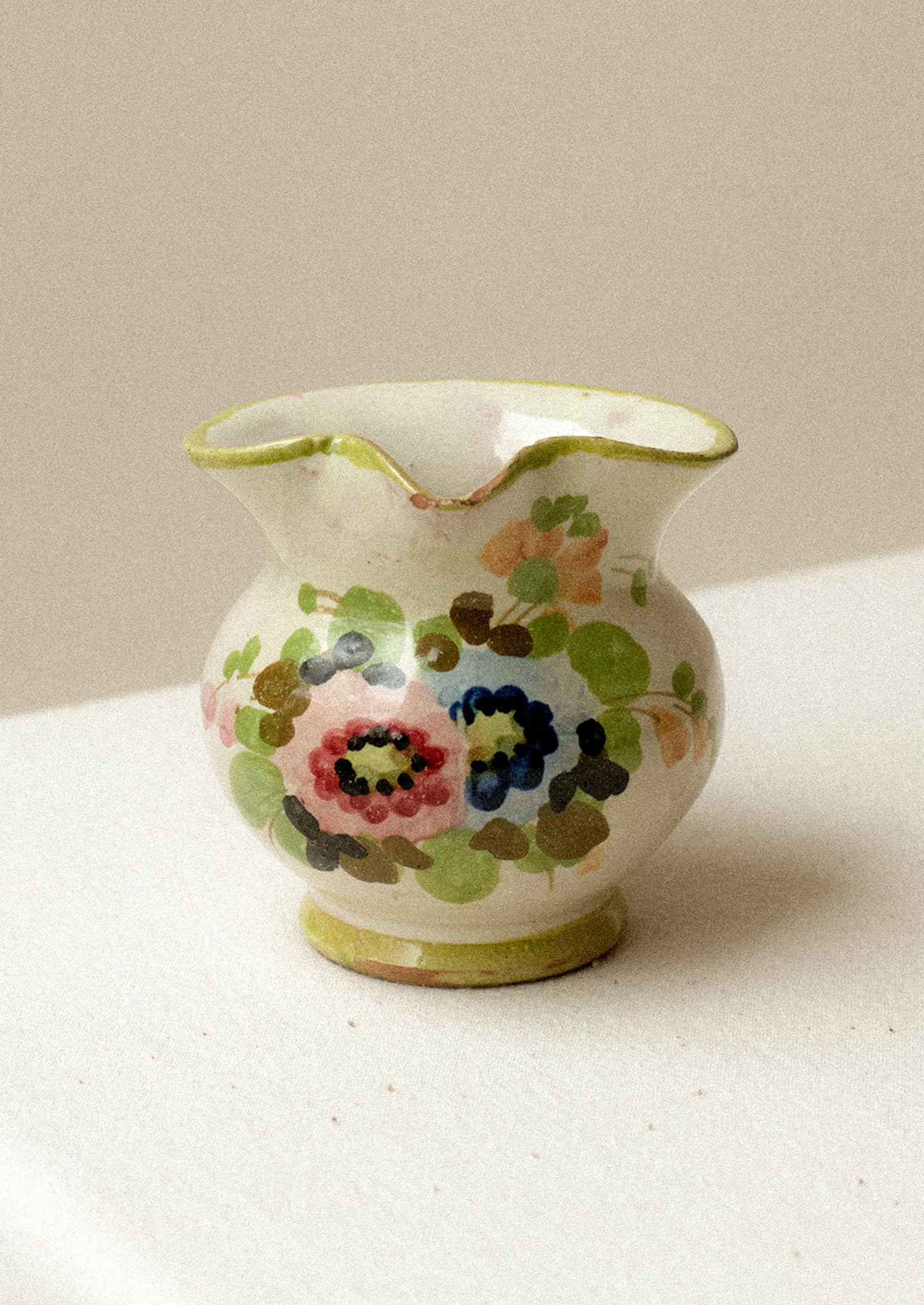 A small ceramic pitcher with painted floral design and green border.