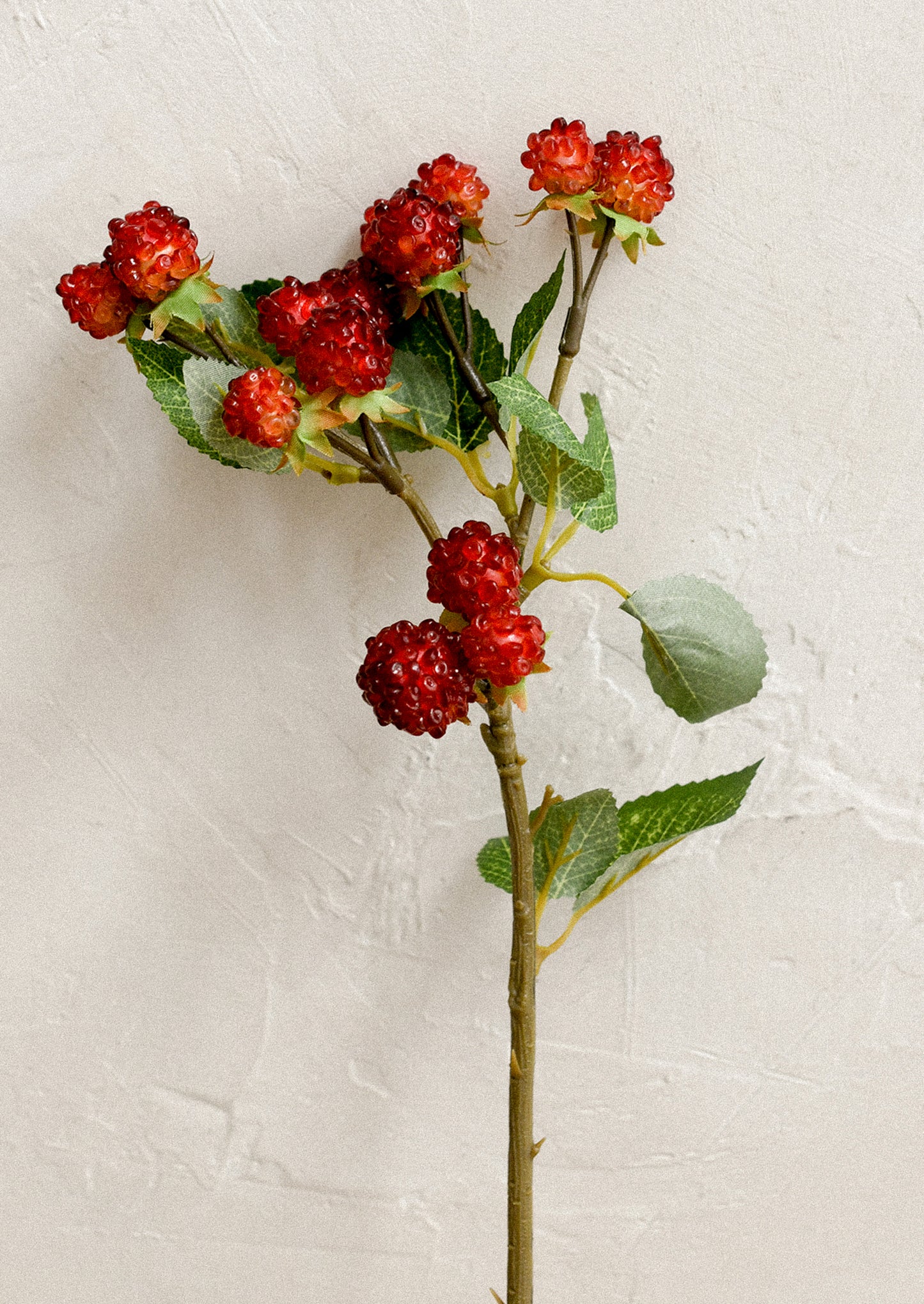 A faux floral stem depicting raspberries on a branch.