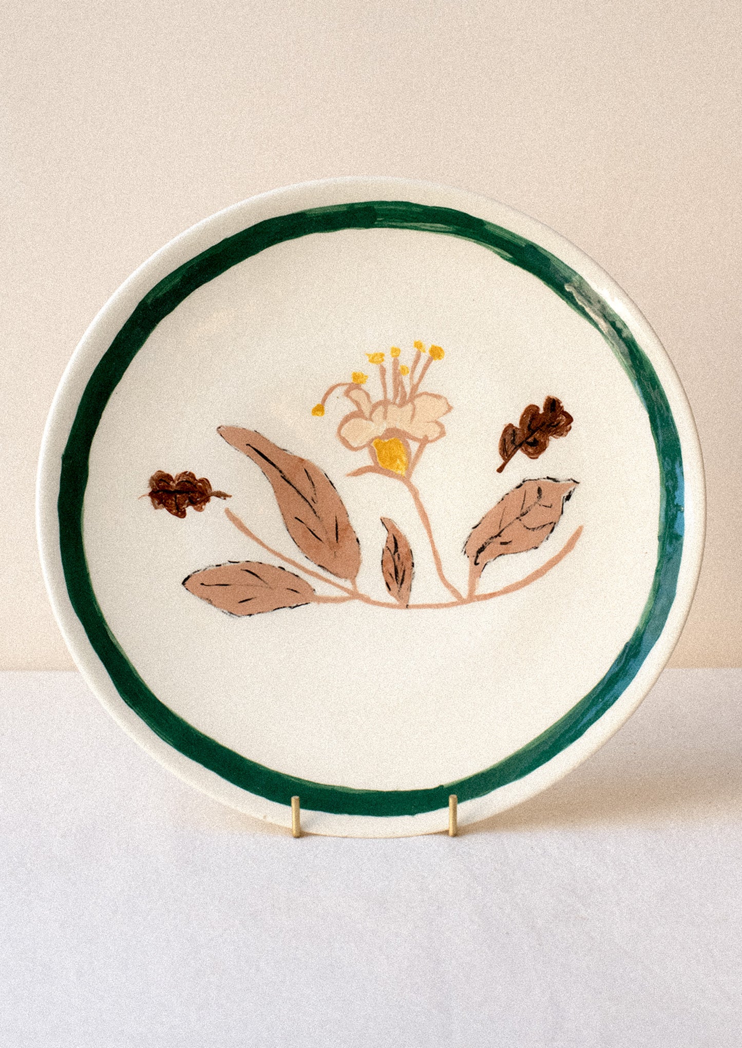 A ceramic plate with hand painted yellow and tan flower and green rim.