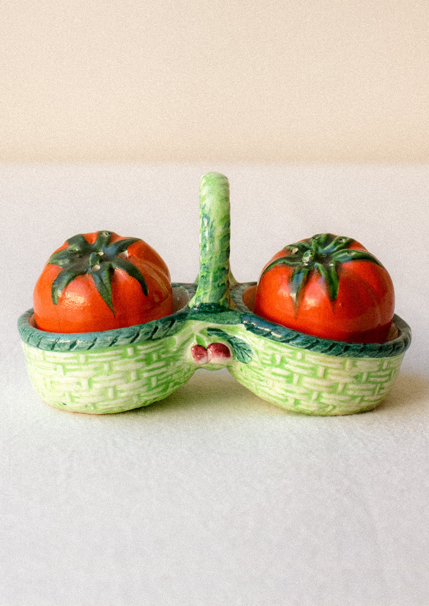 Salt and pepper shakers shaped like tomatoes in a decorative green basket.