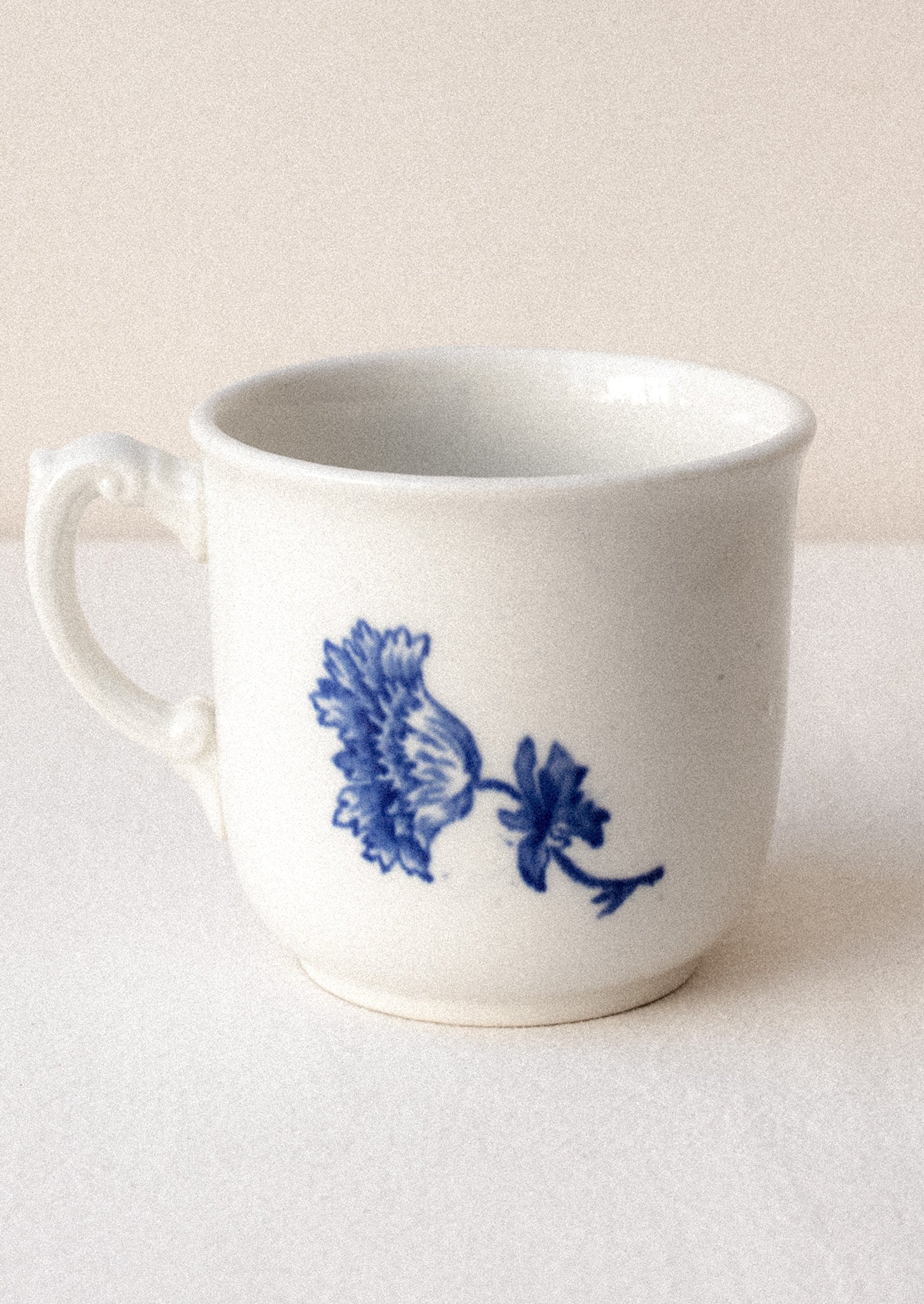 A white mug with flow blue floral pattern and ornate handle.