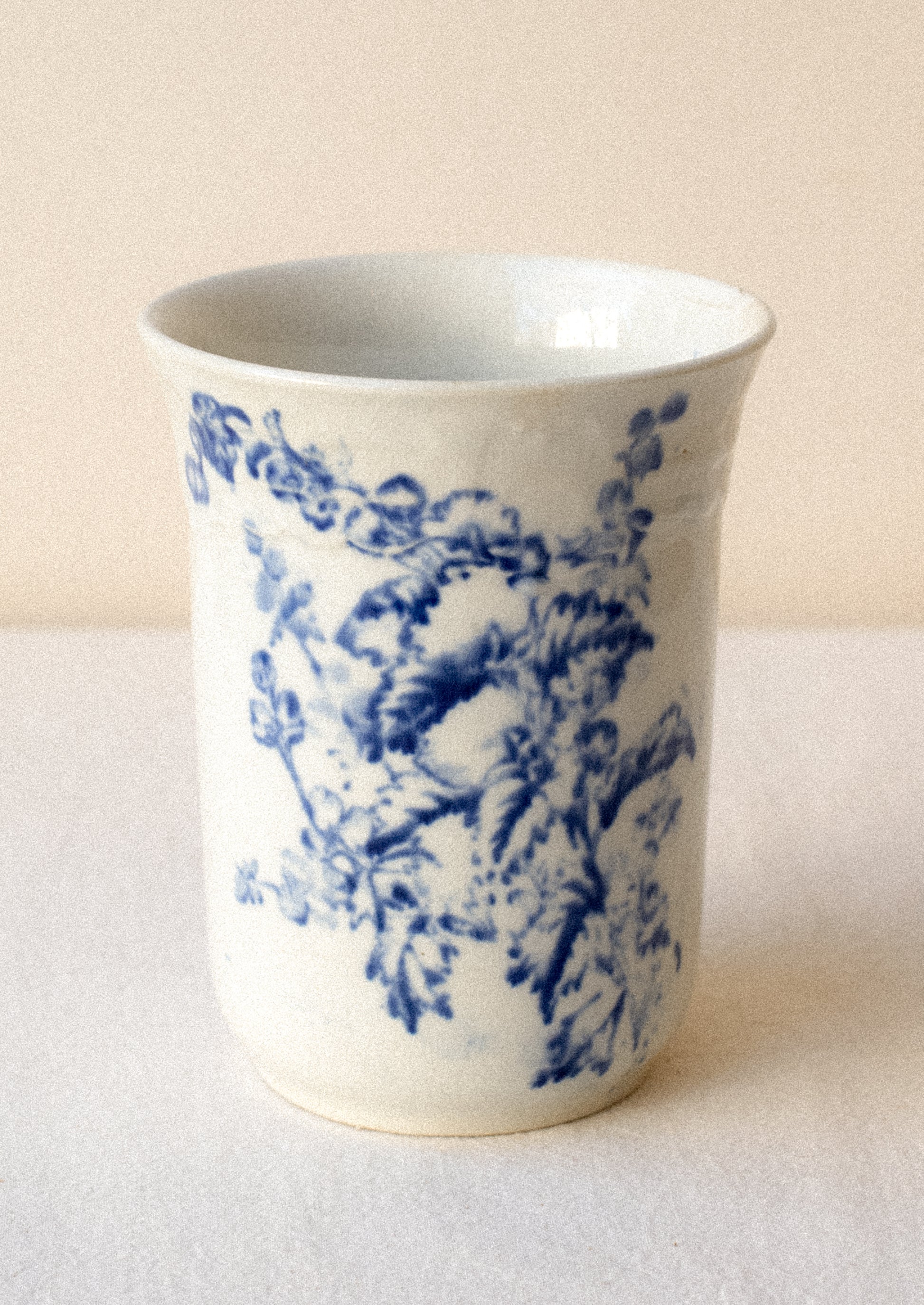 A tall white ceramic cup with flow blue floral pattern.