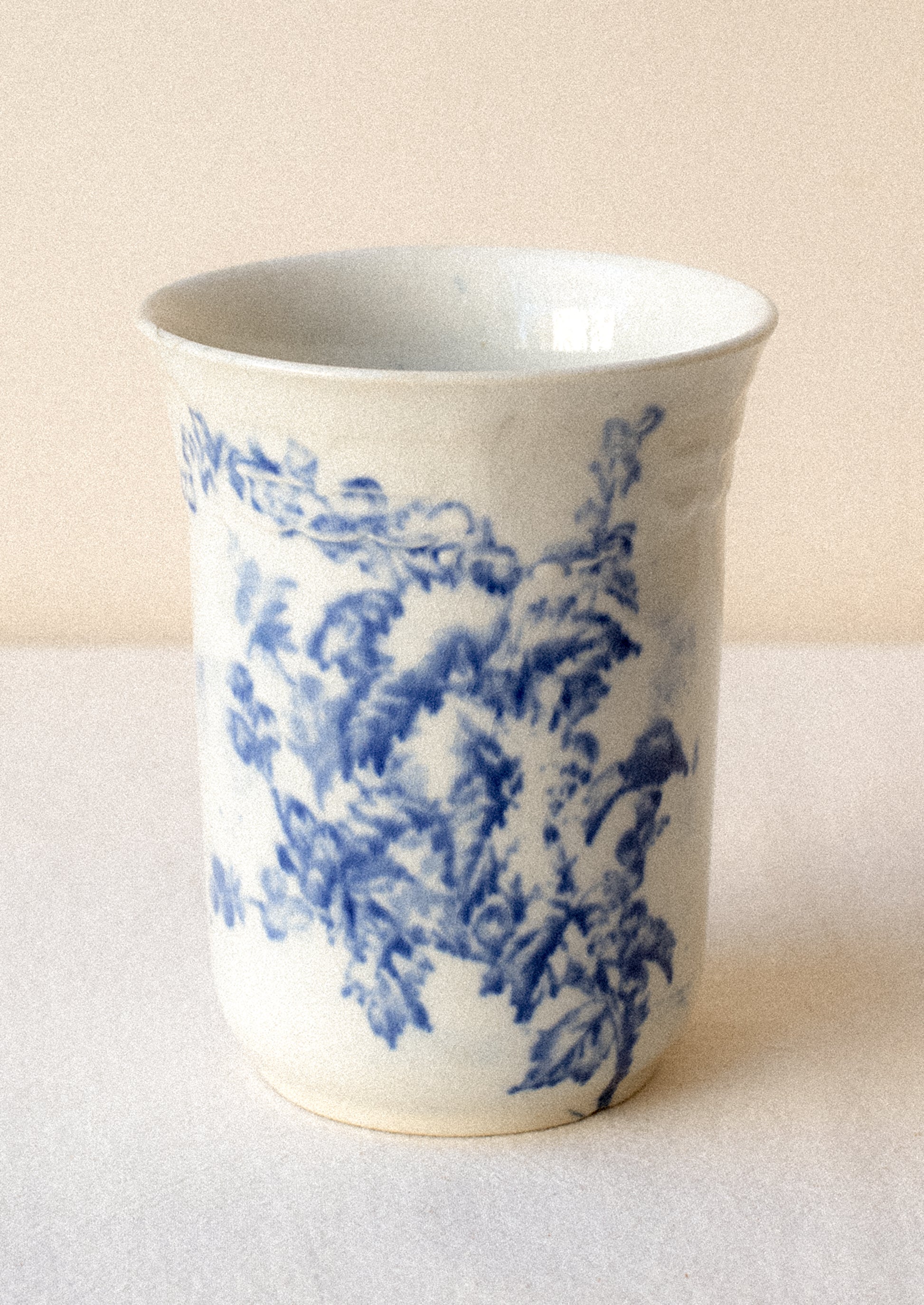 A tall white ceramic cup with flow blue floral pattern.