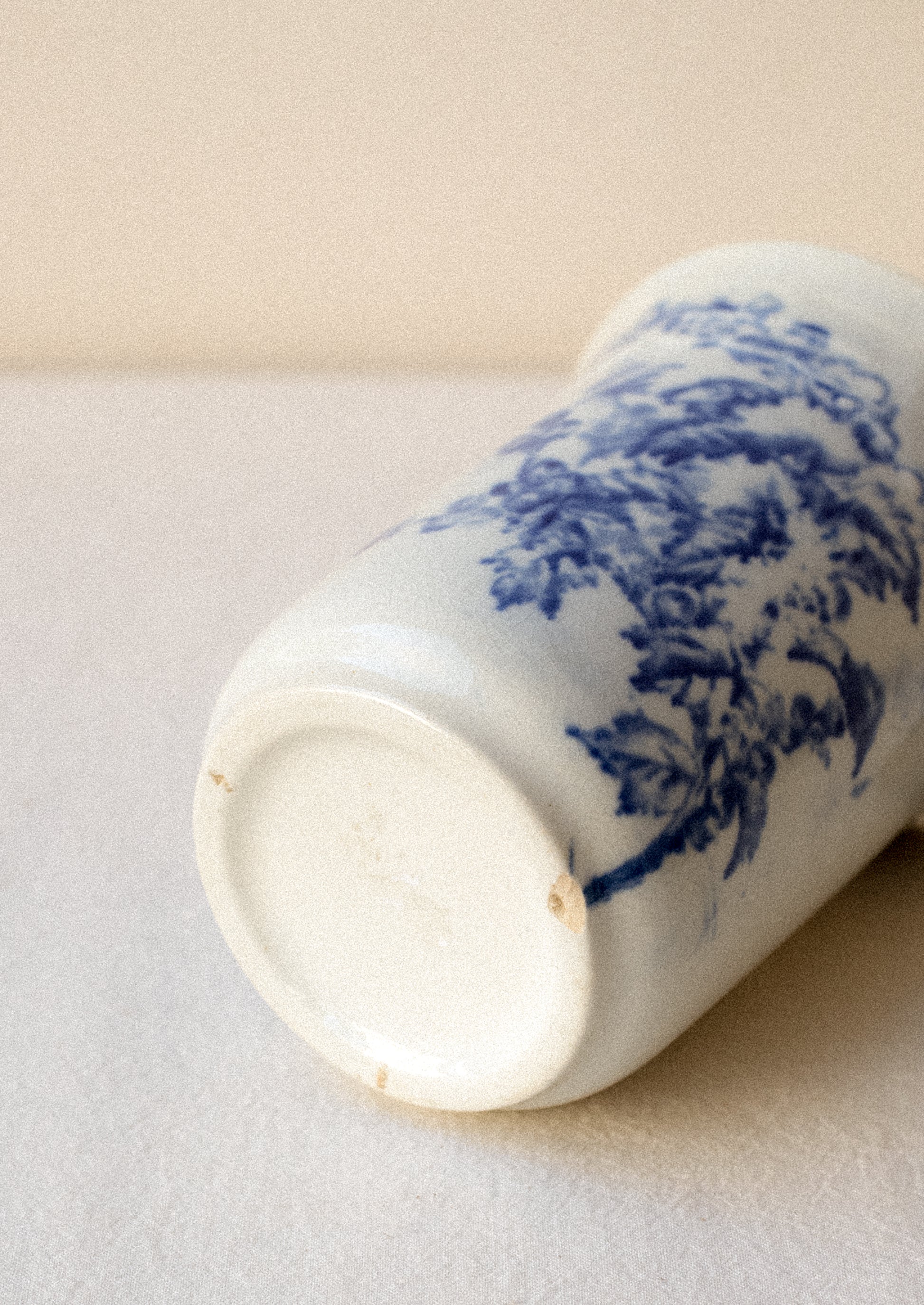 A tall white ceramic cup with flow blue floral pattern.