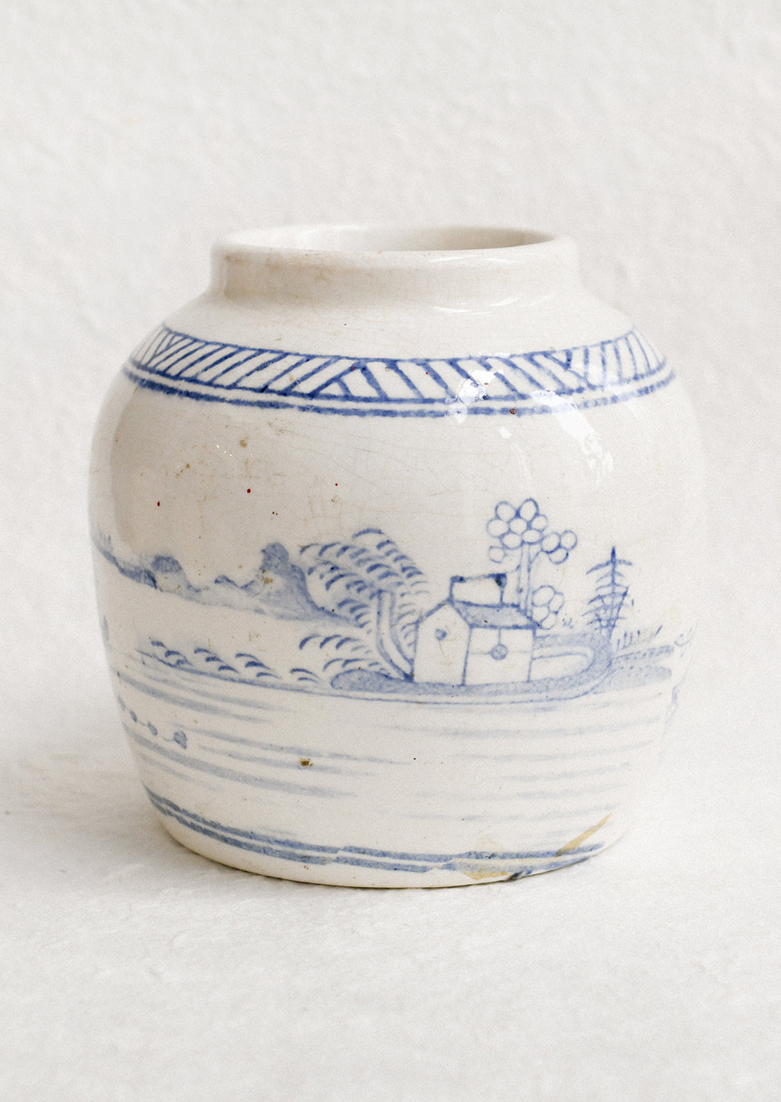 An antique white ginger jar with faded blue painted scene.