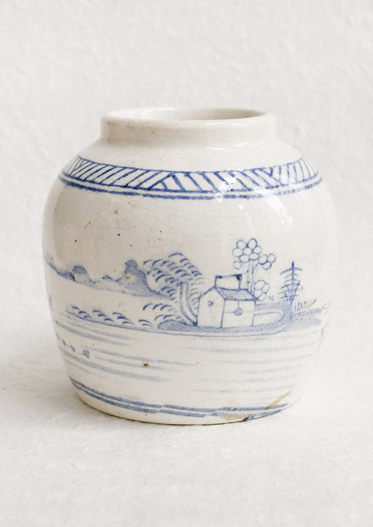 An antique white ginger jar with faded blue painted scene.