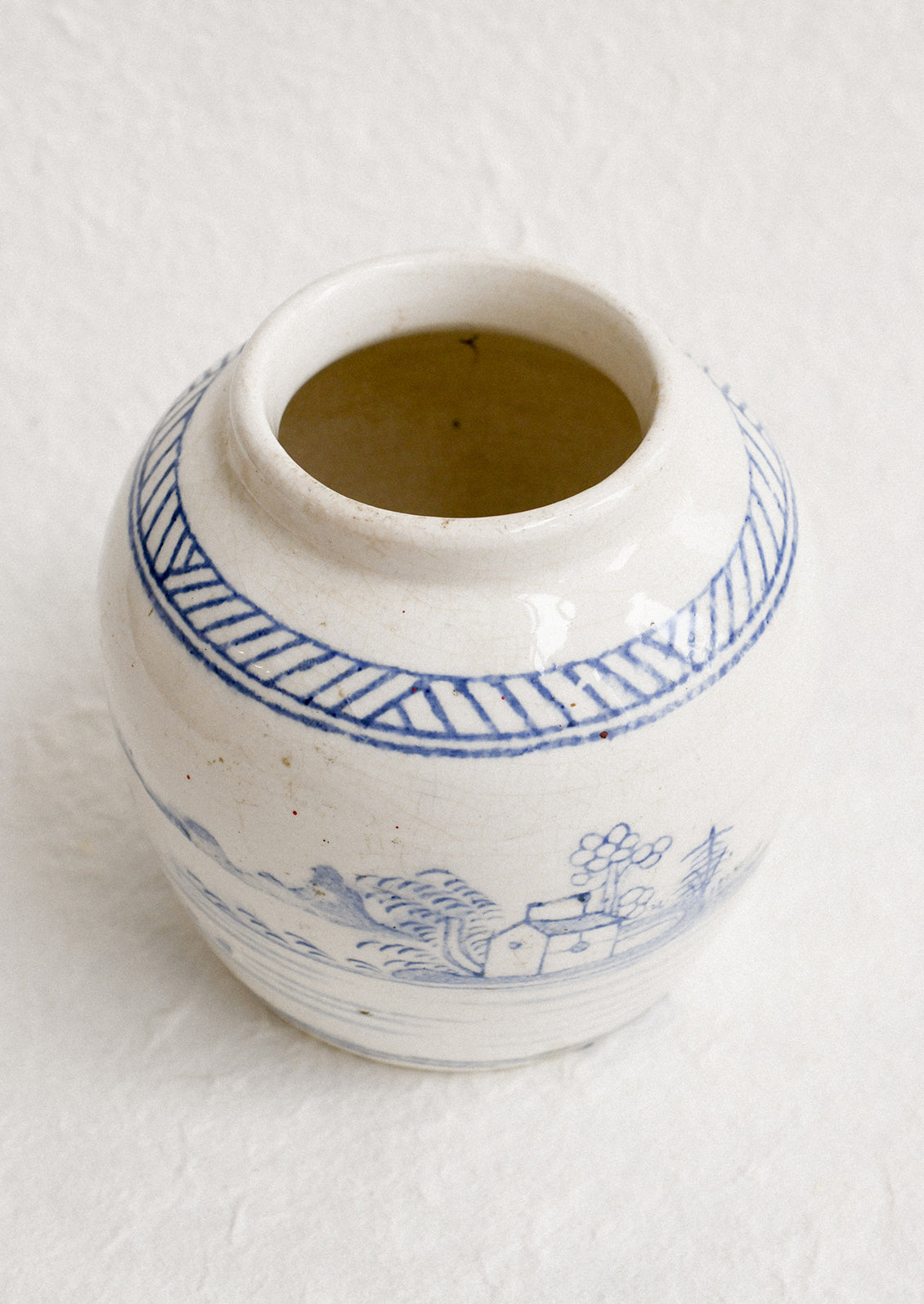 An antique white ginger jar with faded blue painted scene.