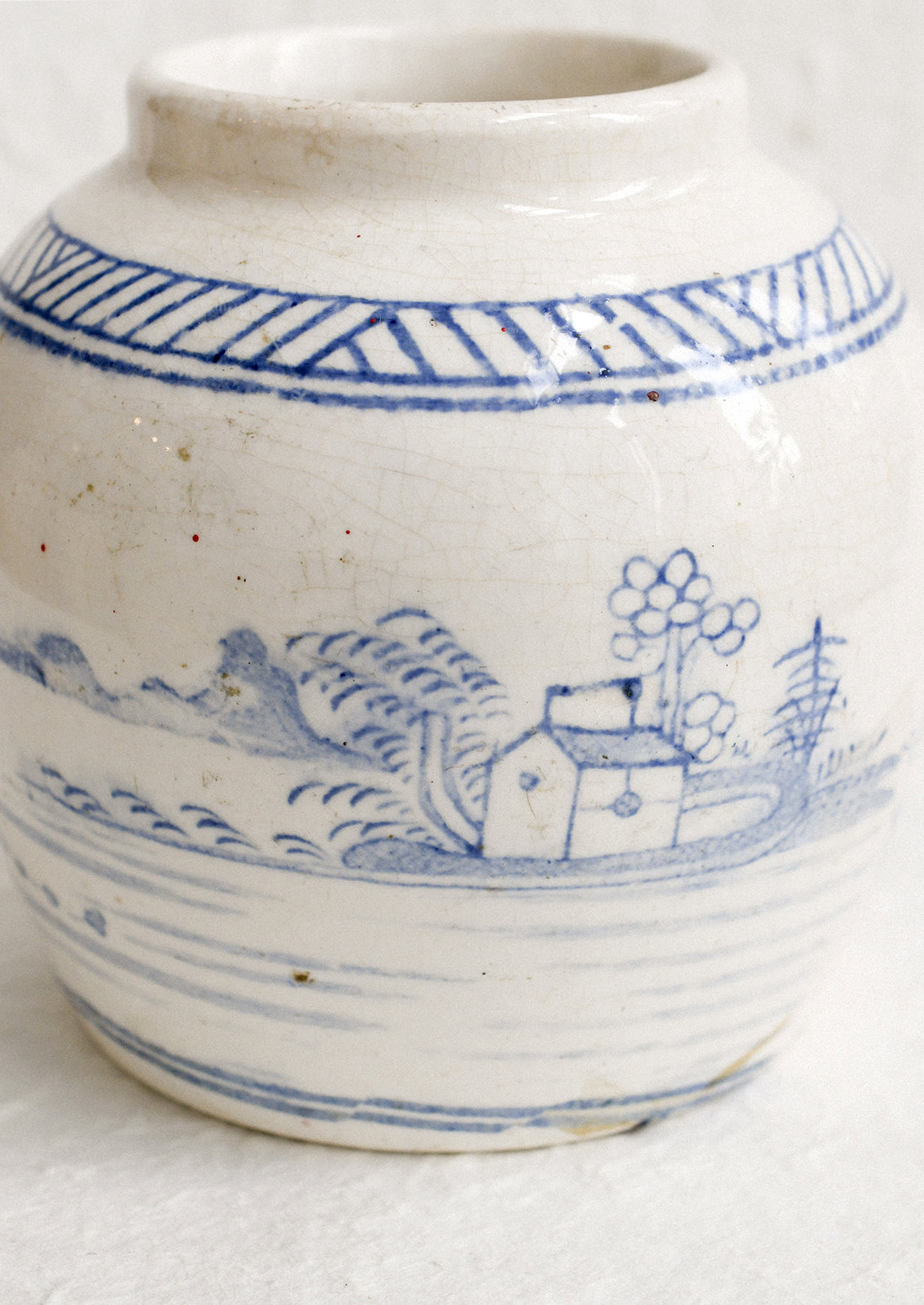 An antique white ginger jar with faded blue painted scene.