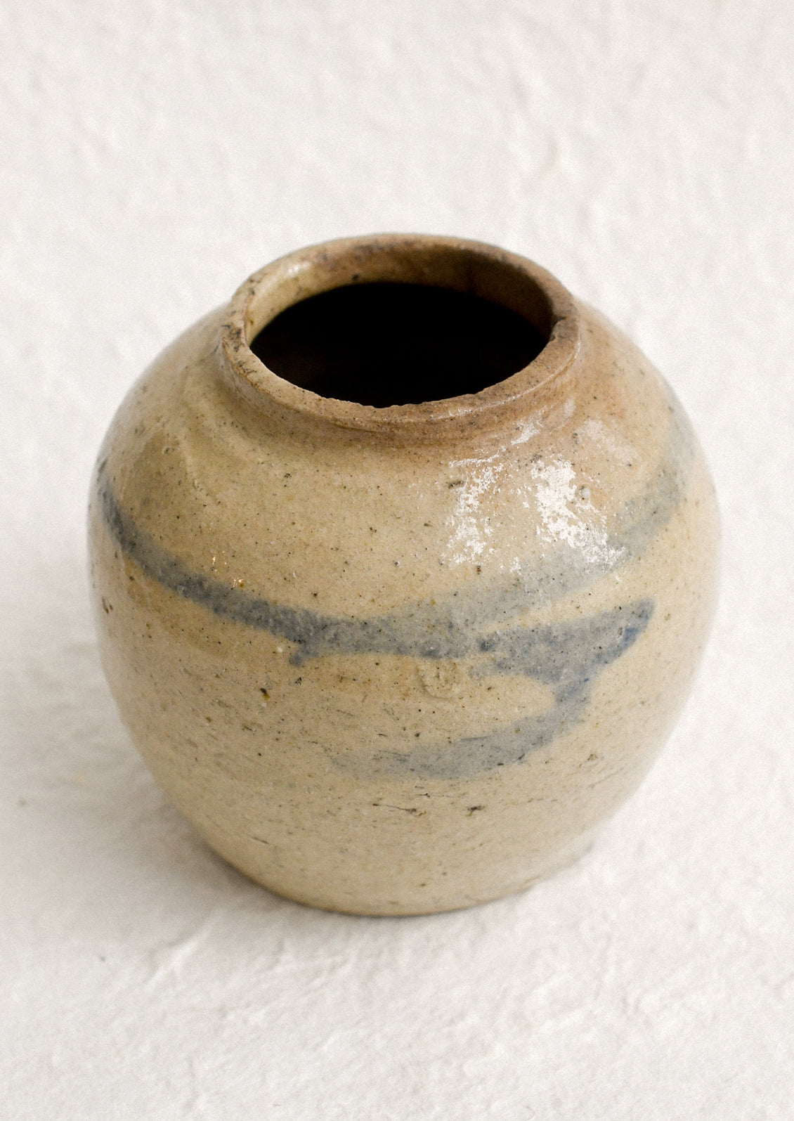 A small antique ginger jar in distressed tan ceramic with pale blue stripes.