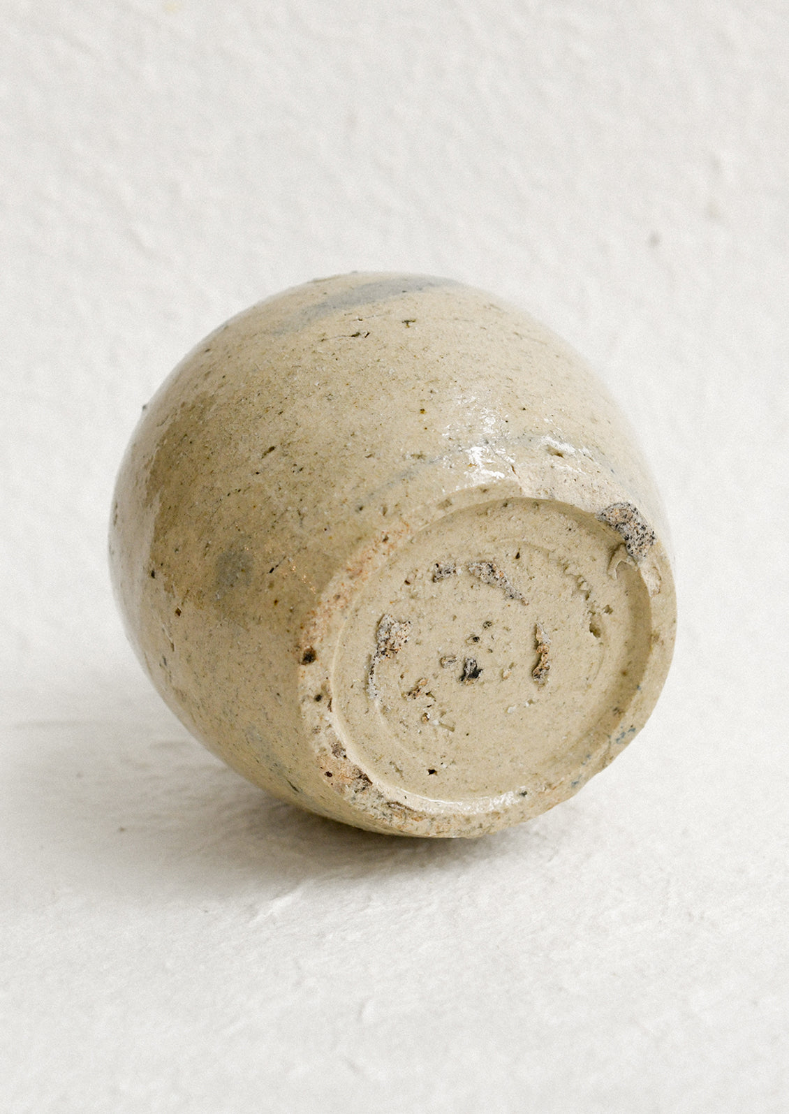 A small antique ginger jar in distressed tan ceramic with pale blue stripes.