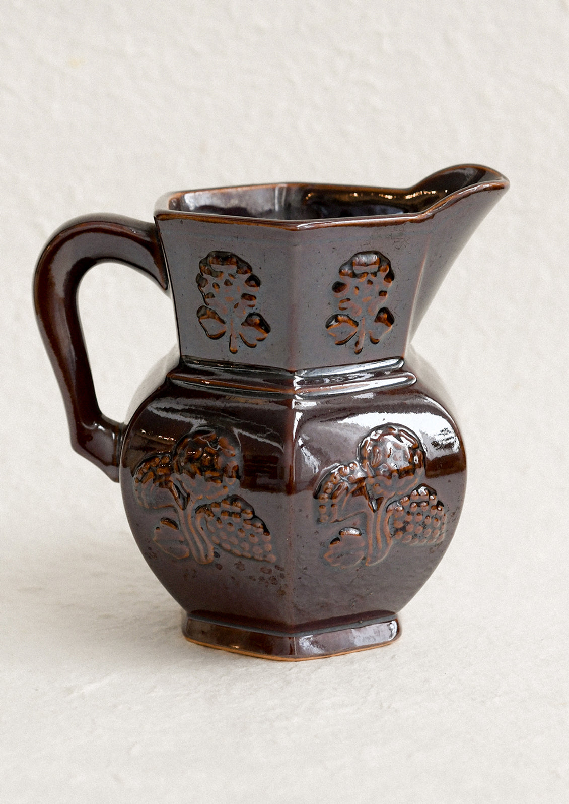 A dark brown pitcher with iridescent glaze and embossed floral pattern.