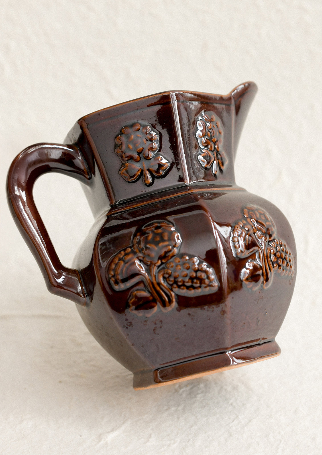 A dark brown pitcher with iridescent glaze and embossed floral pattern.