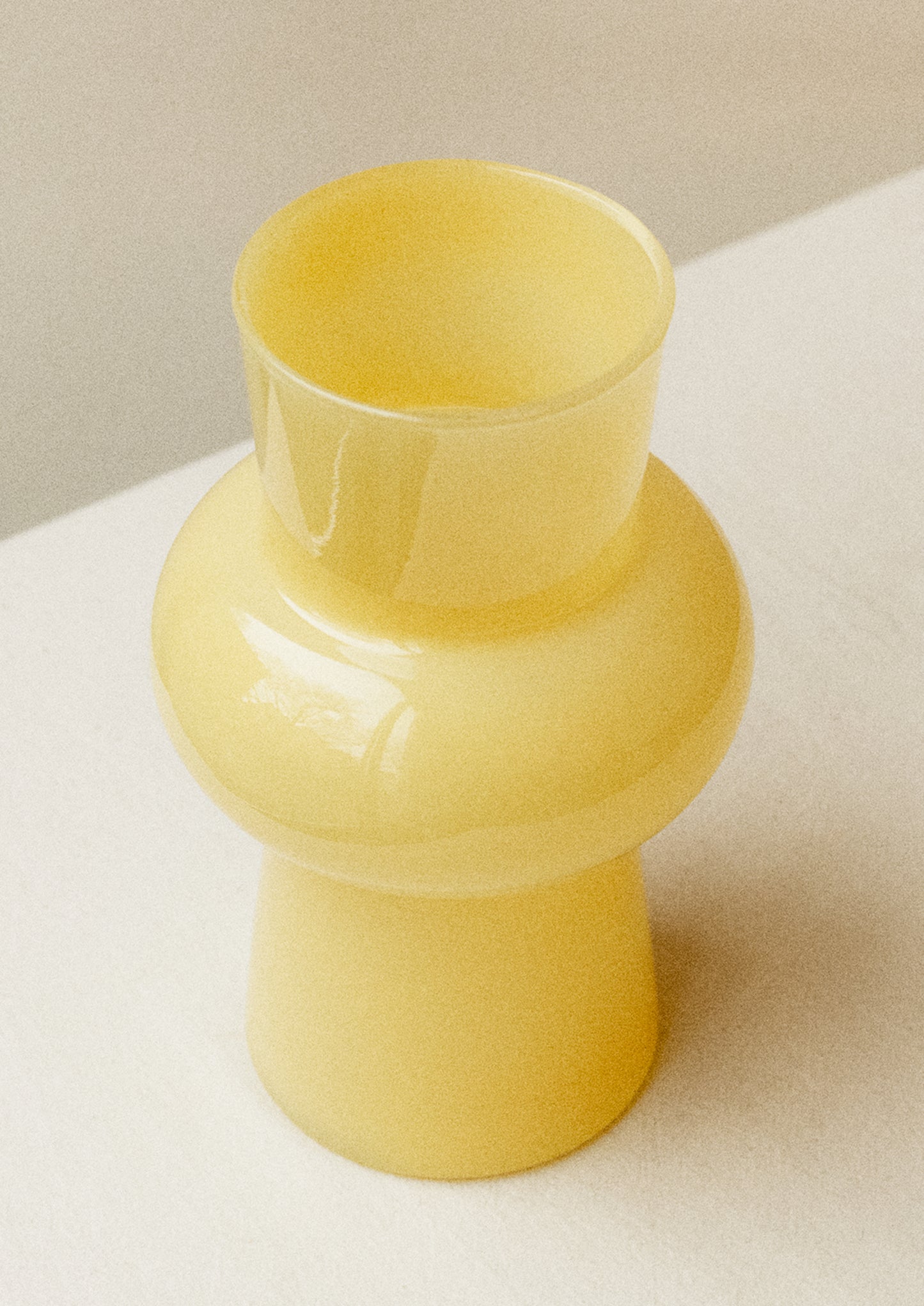 A glass vase with bulbous middle in opaque butter yellow hue.