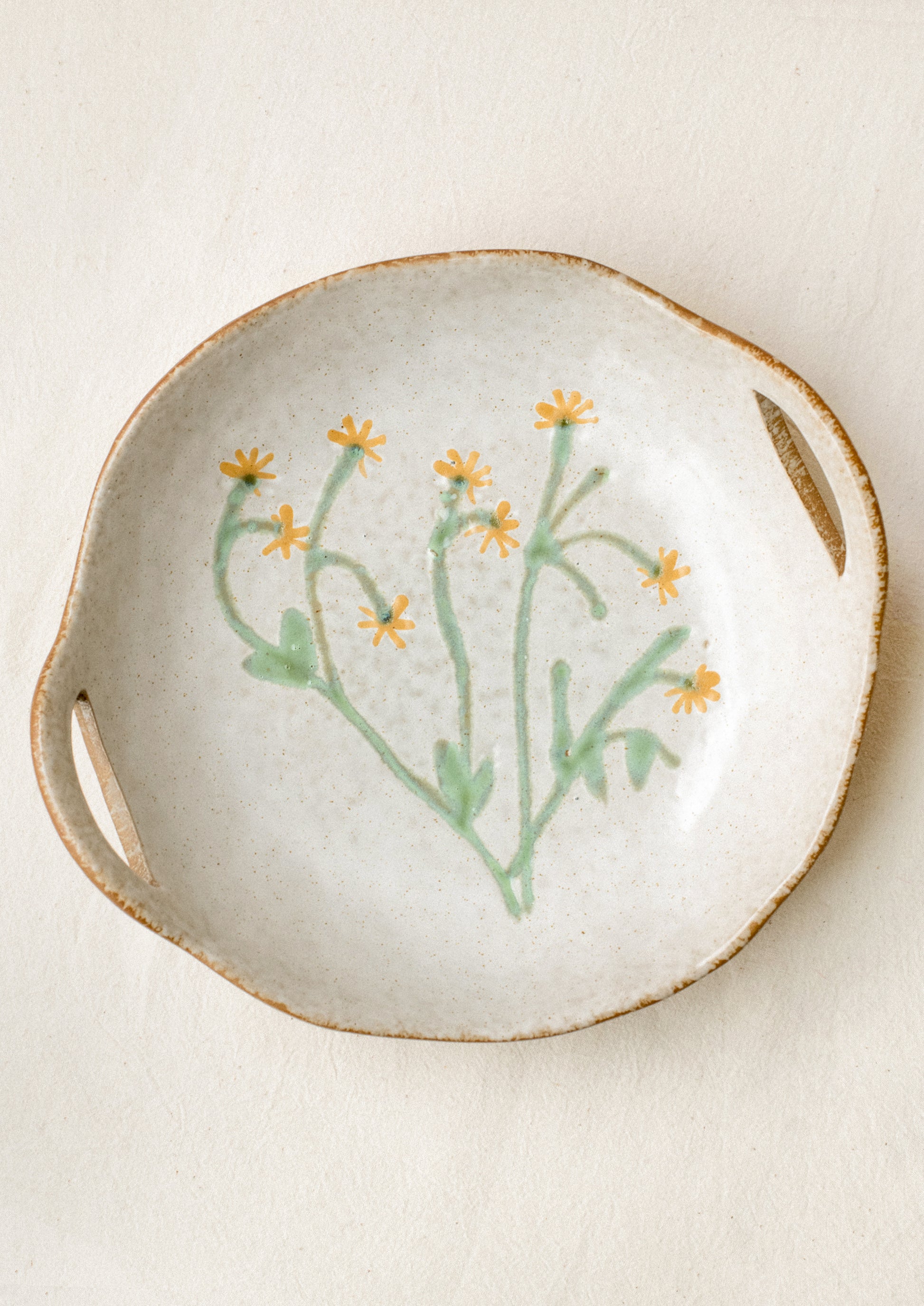 A ceramic serving bowl with cutout side handles and yellow painted flower at center.