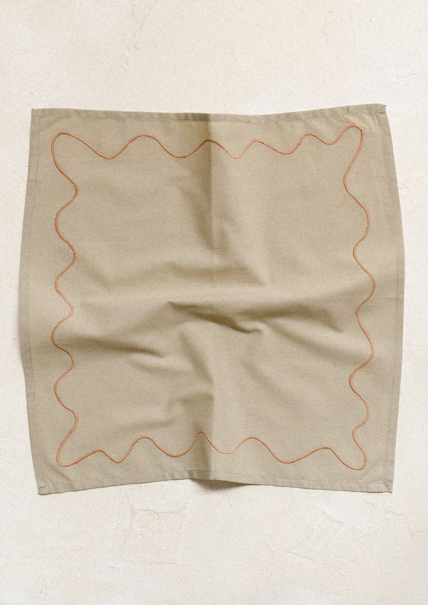 A pair of greige napkins with peach squiggle embroidery.