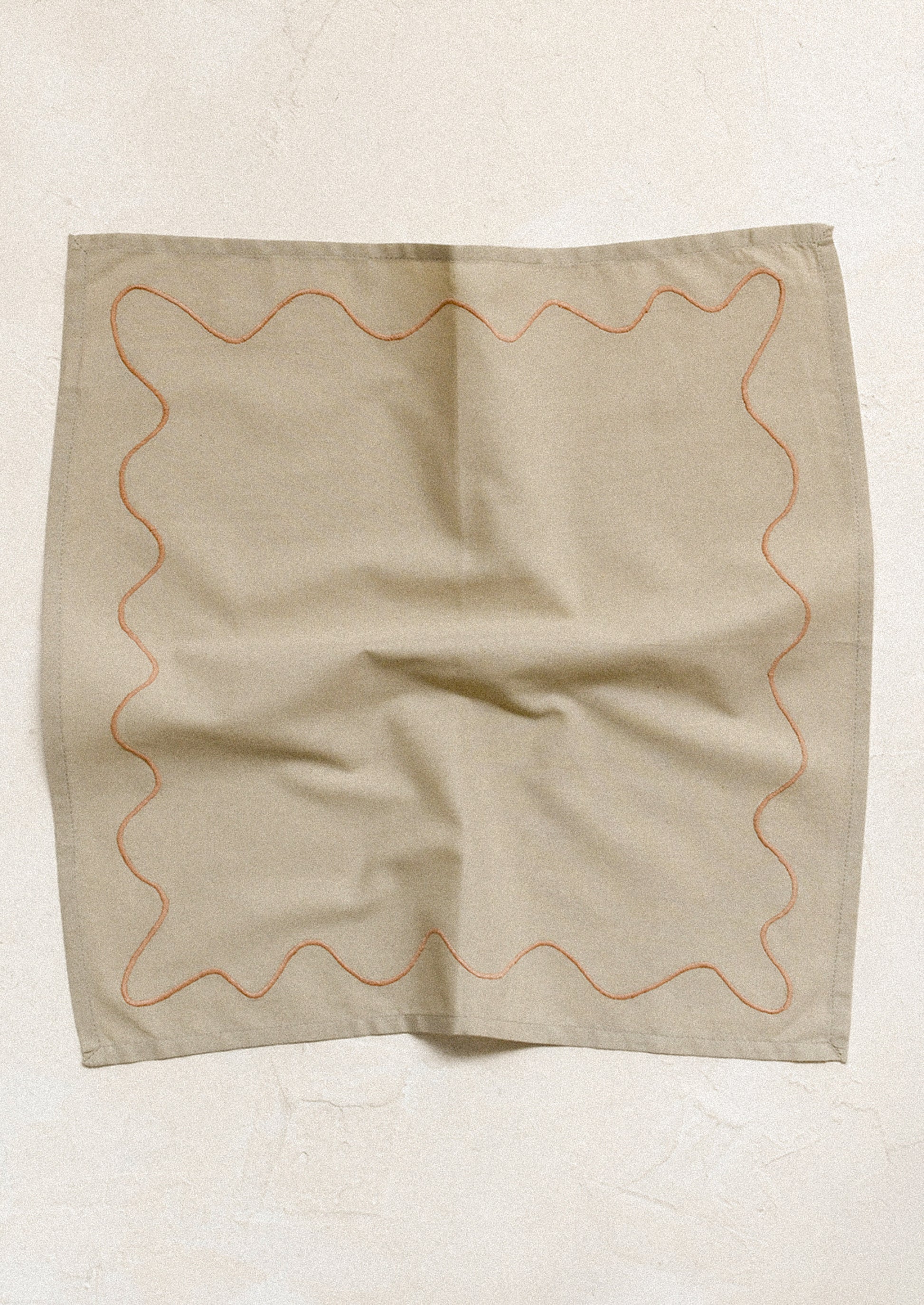 A pair of greige napkins with peach squiggle embroidery.