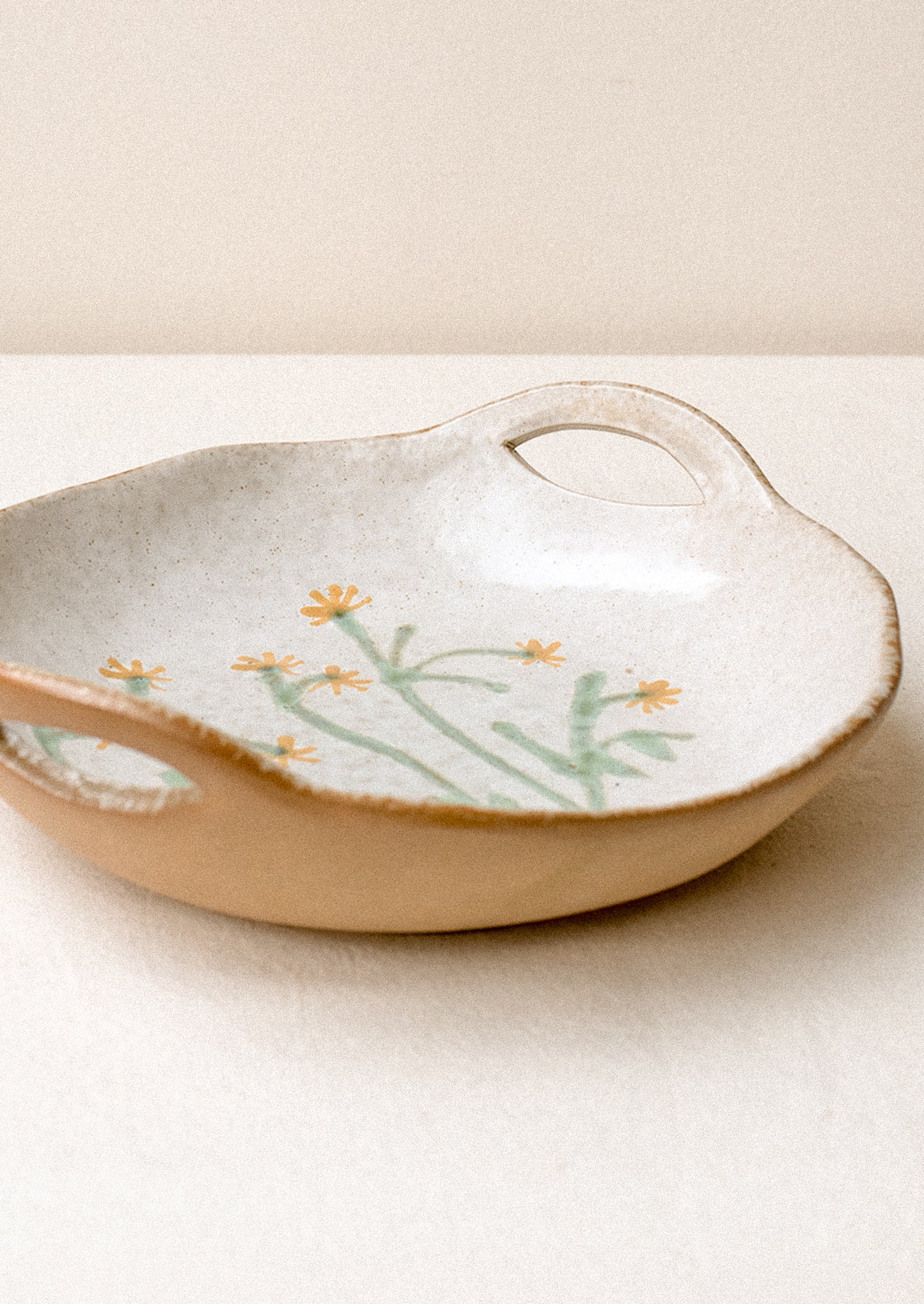 A ceramic serving bowl with cutout side handles and yellow painted flower at center.