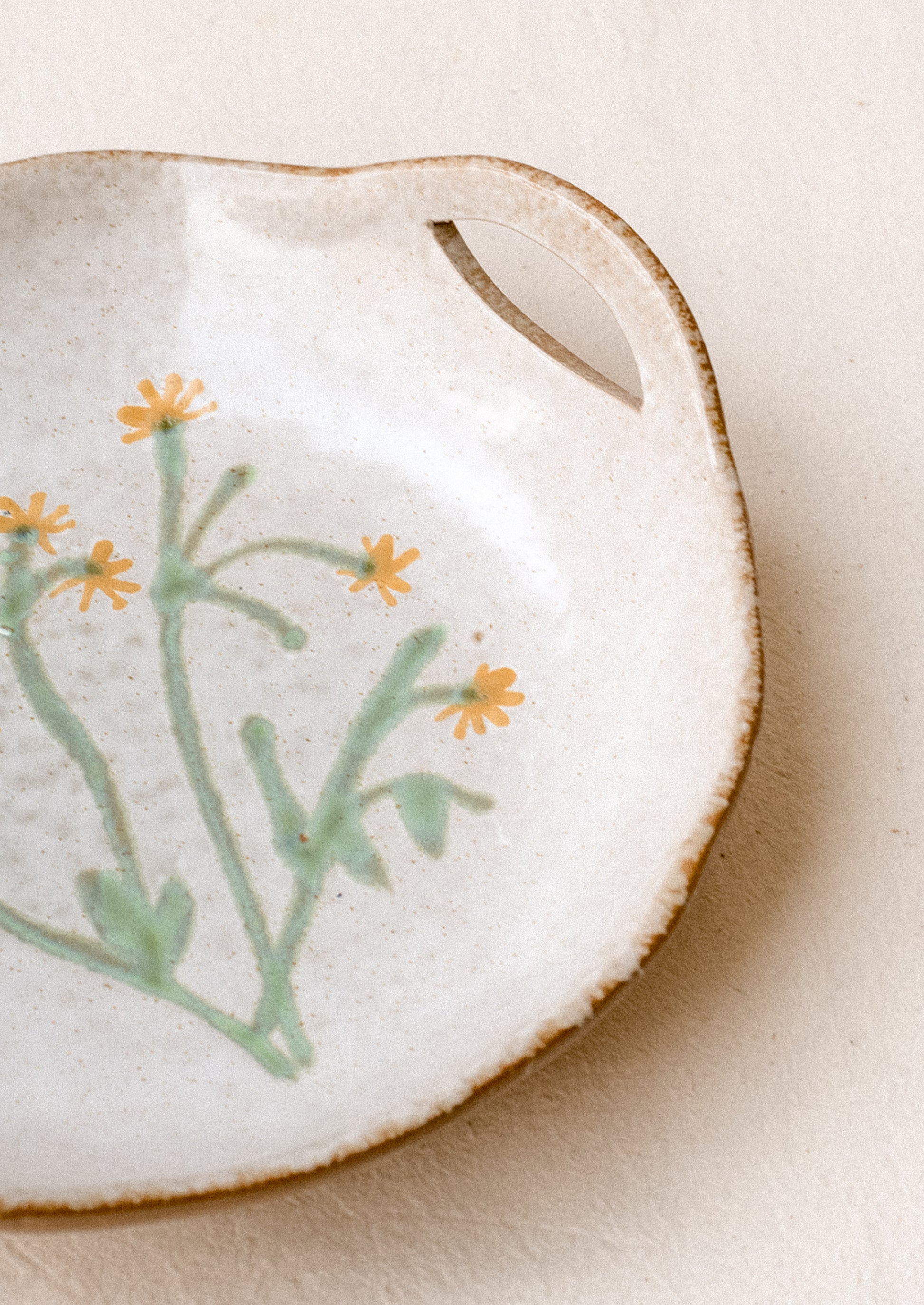A ceramic serving bowl with cutout side handles and yellow painted flower at center.