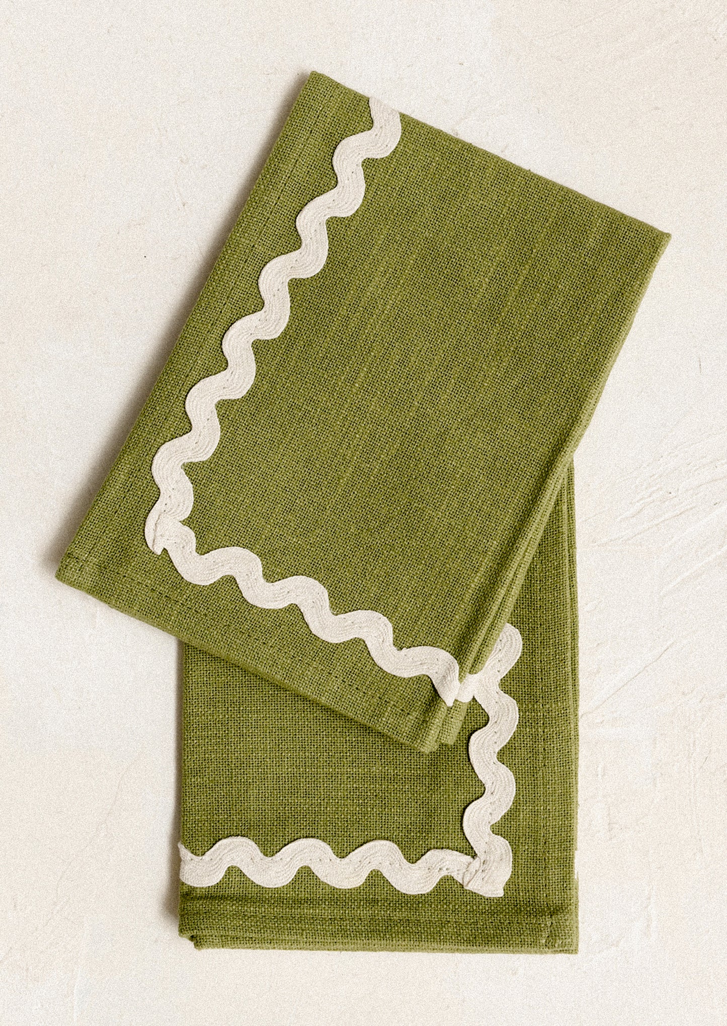 A pair of olive green napkins with white ricrac border.