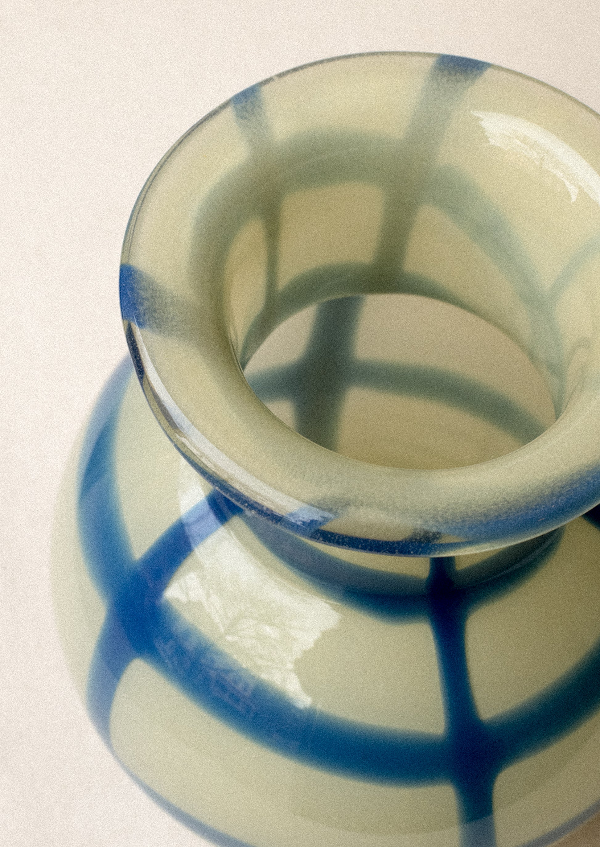 A glass vase with round shape, in yellow with painted blue gingham pattern.