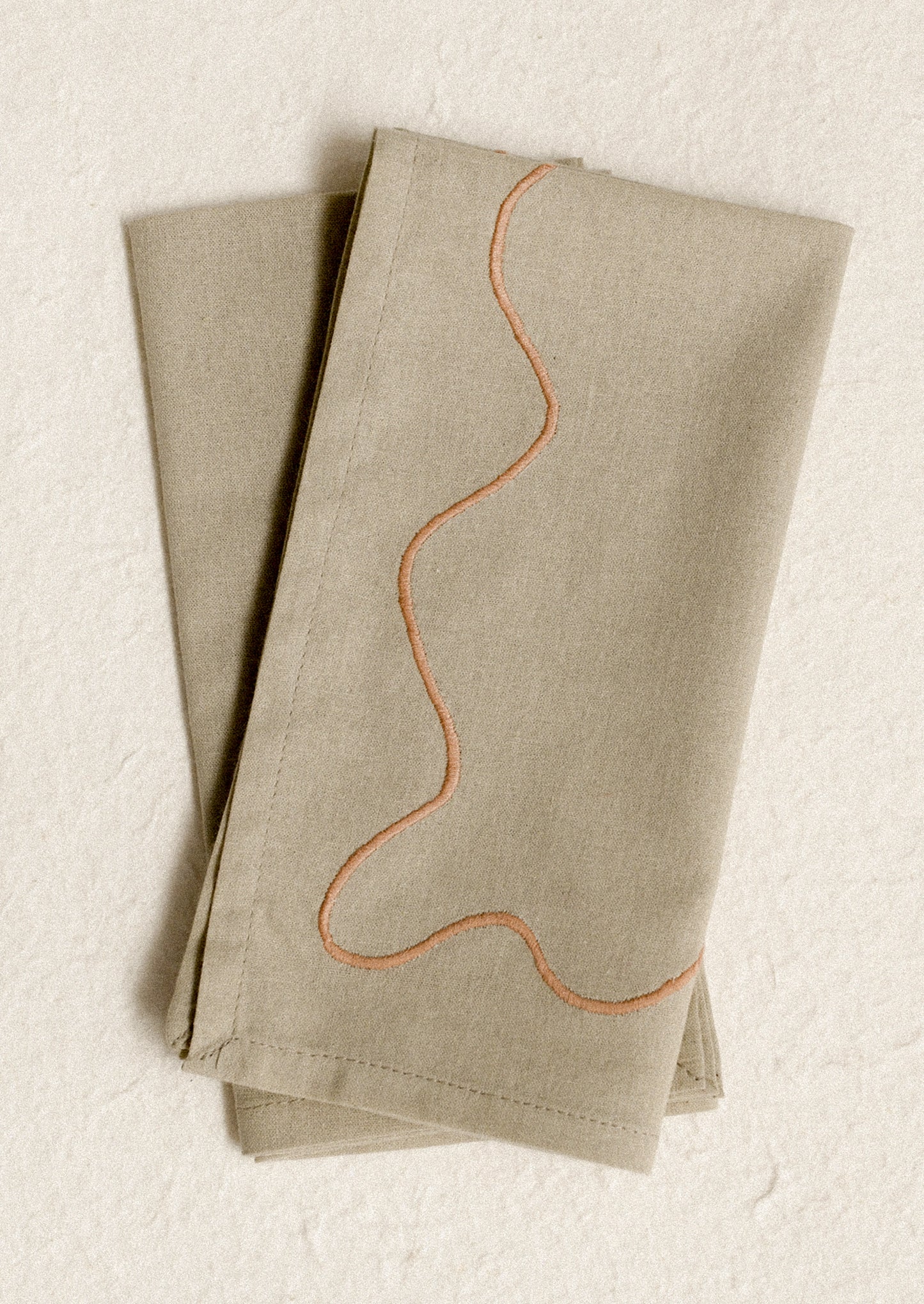 A pair of greige napkins with peach squiggle embroidery.