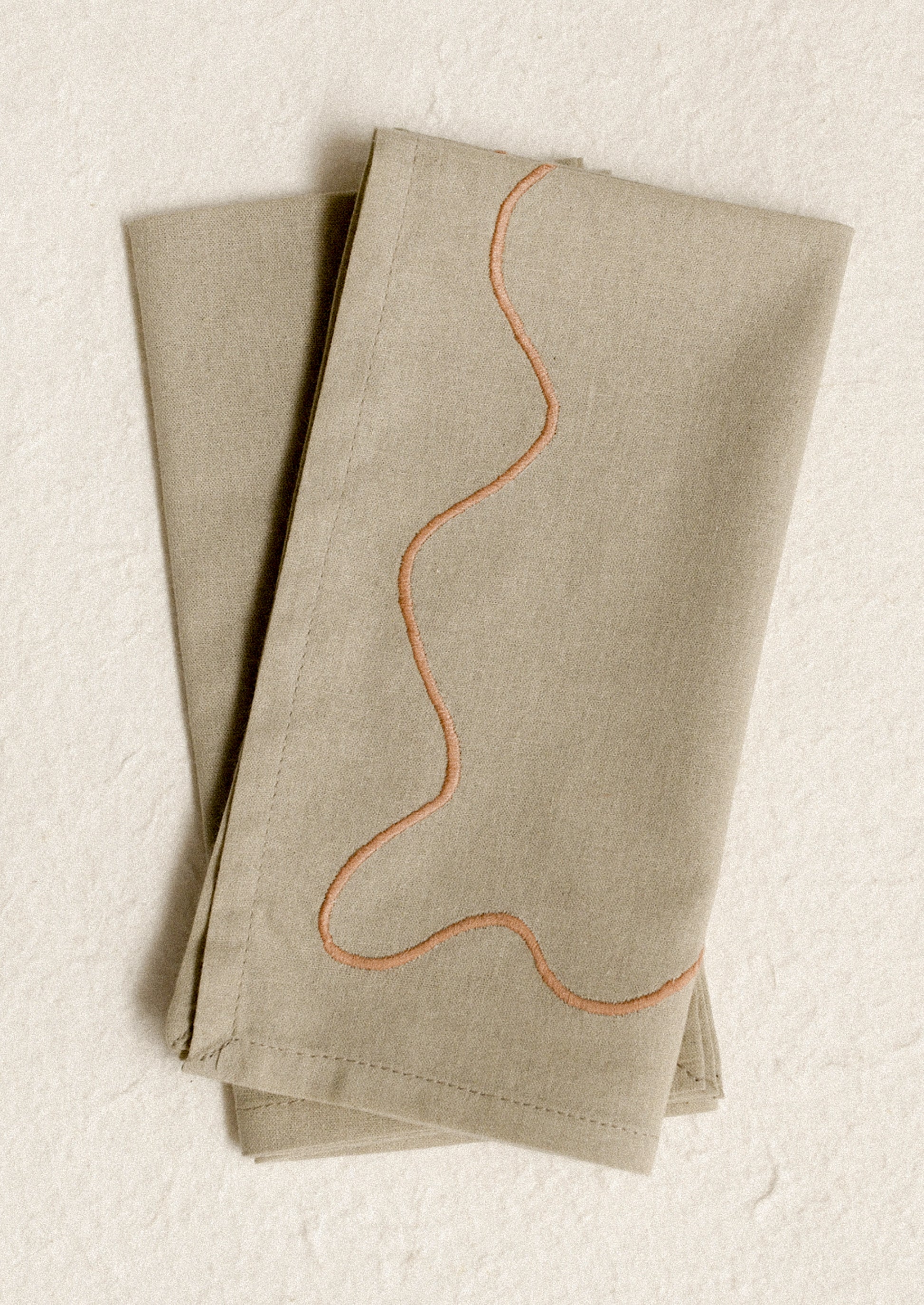 A pair of greige napkins with peach squiggle embroidery.