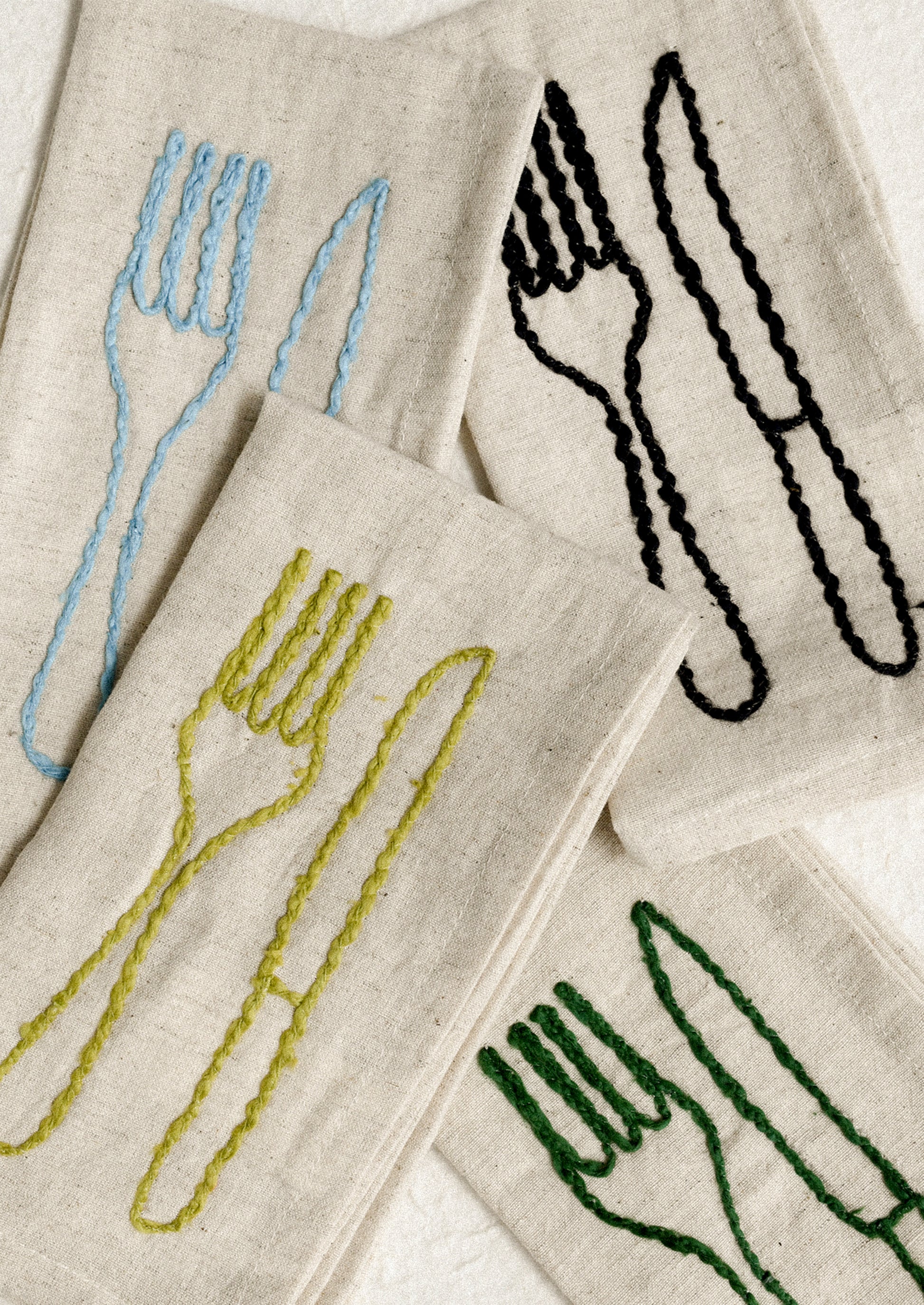 A set of natural linen napkins with embroidered fork and knife motif in assorted colors.
