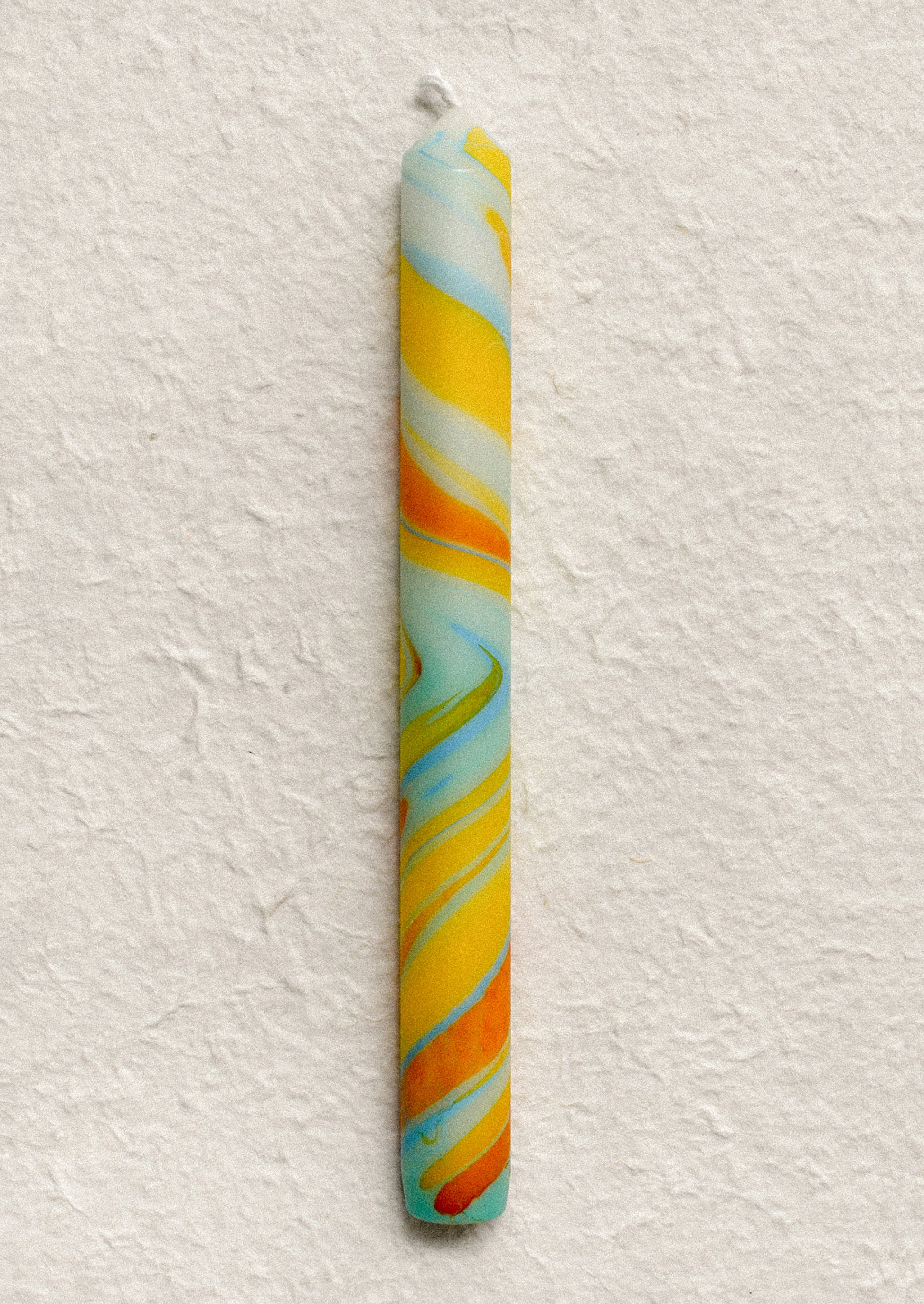 A marbled taper candle in blue, orange and yellow swirl pattern.