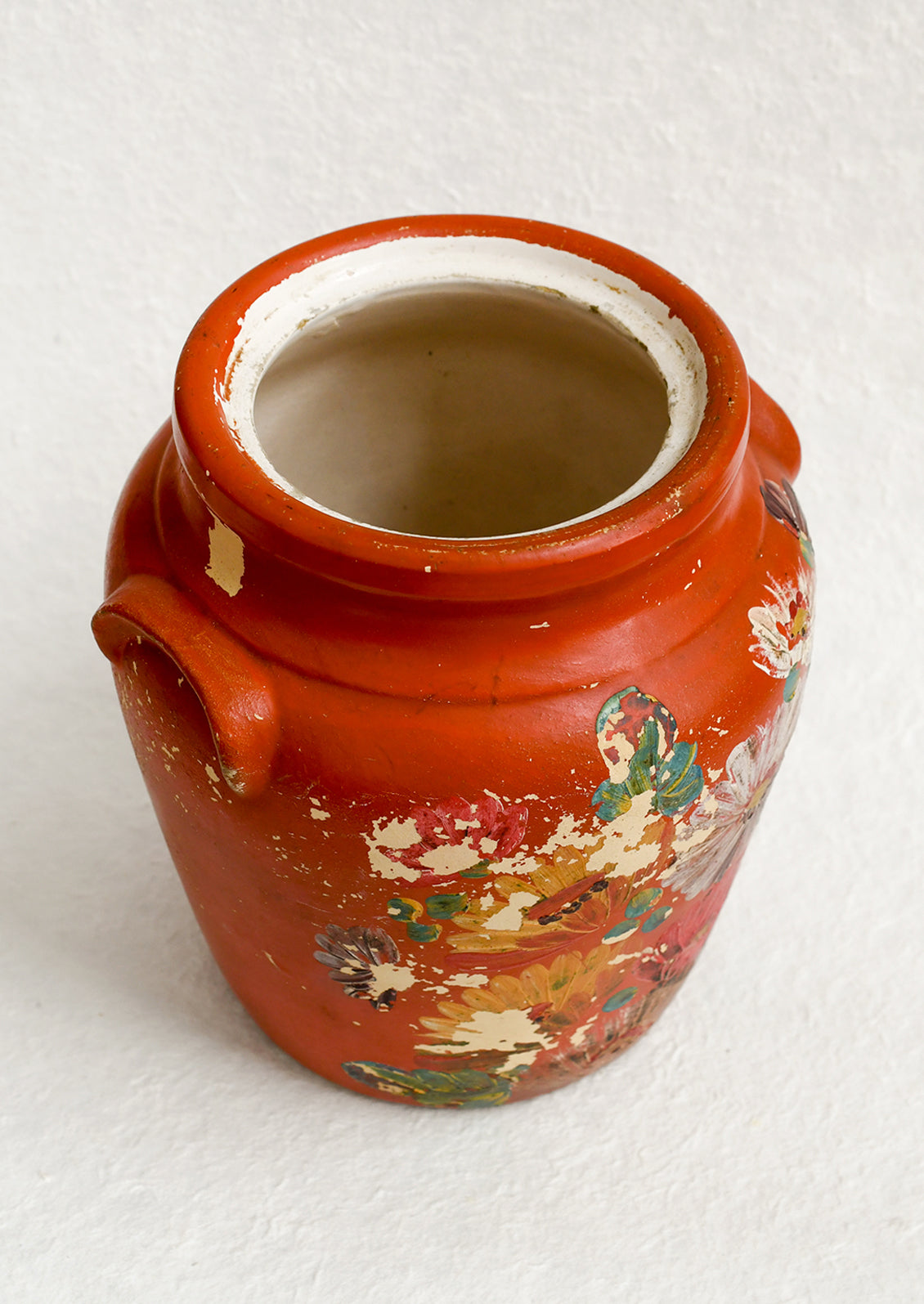 An antique cookie jar in red with chippy floral painted design.
