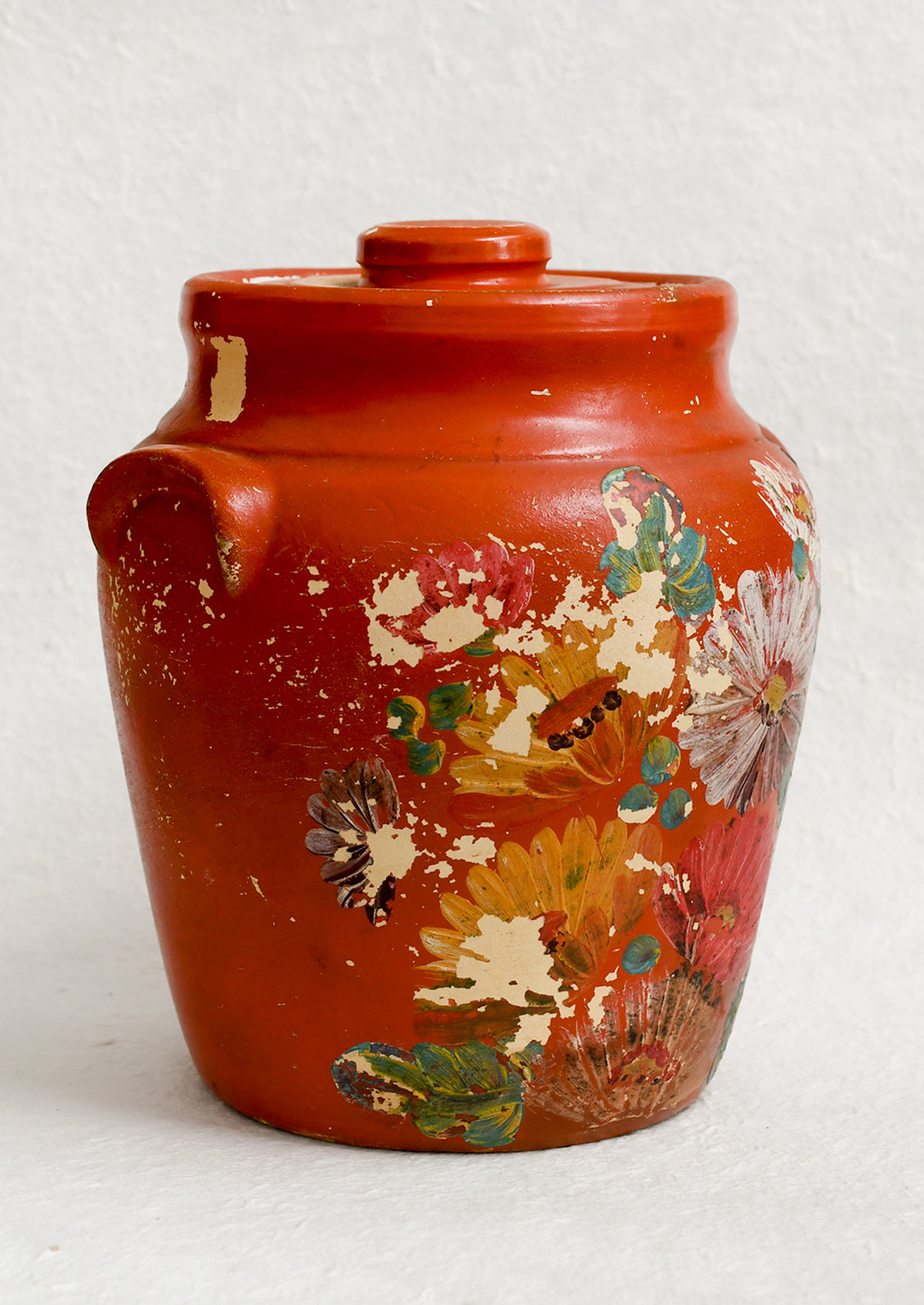 An antique cookie jar in red with chippy floral painted design.