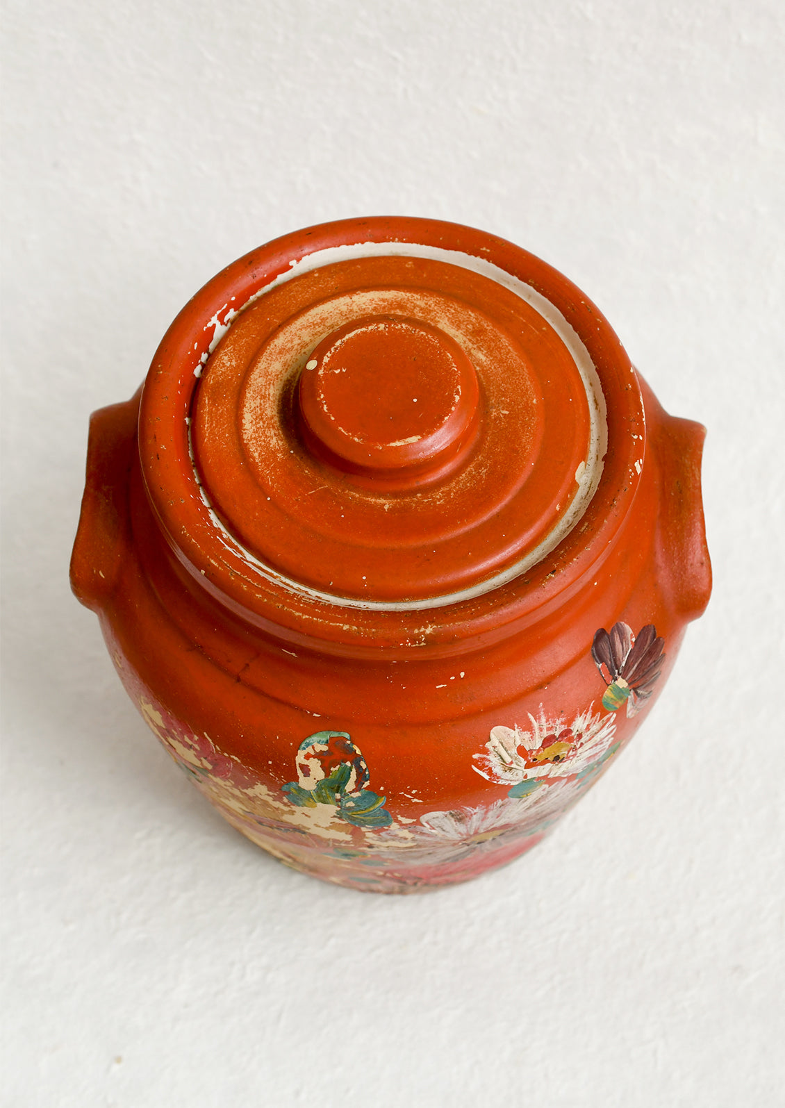 An antique cookie jar in red with chippy floral painted design.