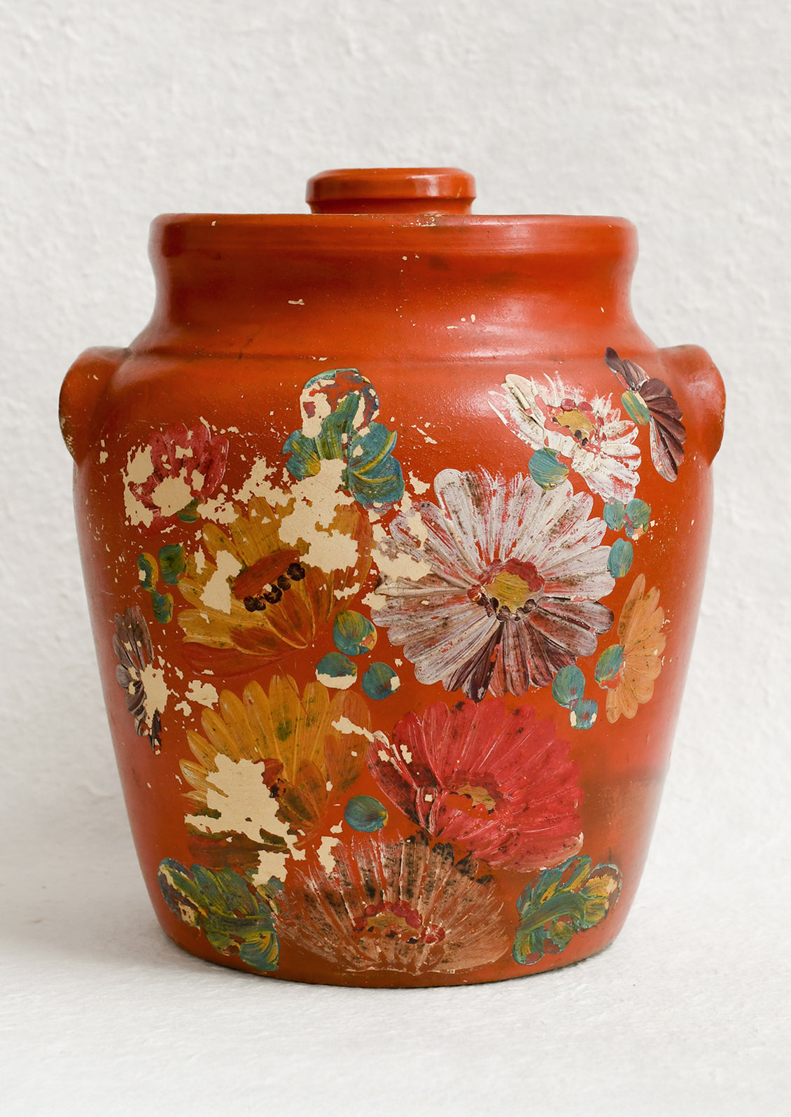 An antique cookie jar in red with chippy floral painted design.