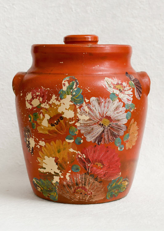 An antique cookie jar in red with chippy floral painted design.