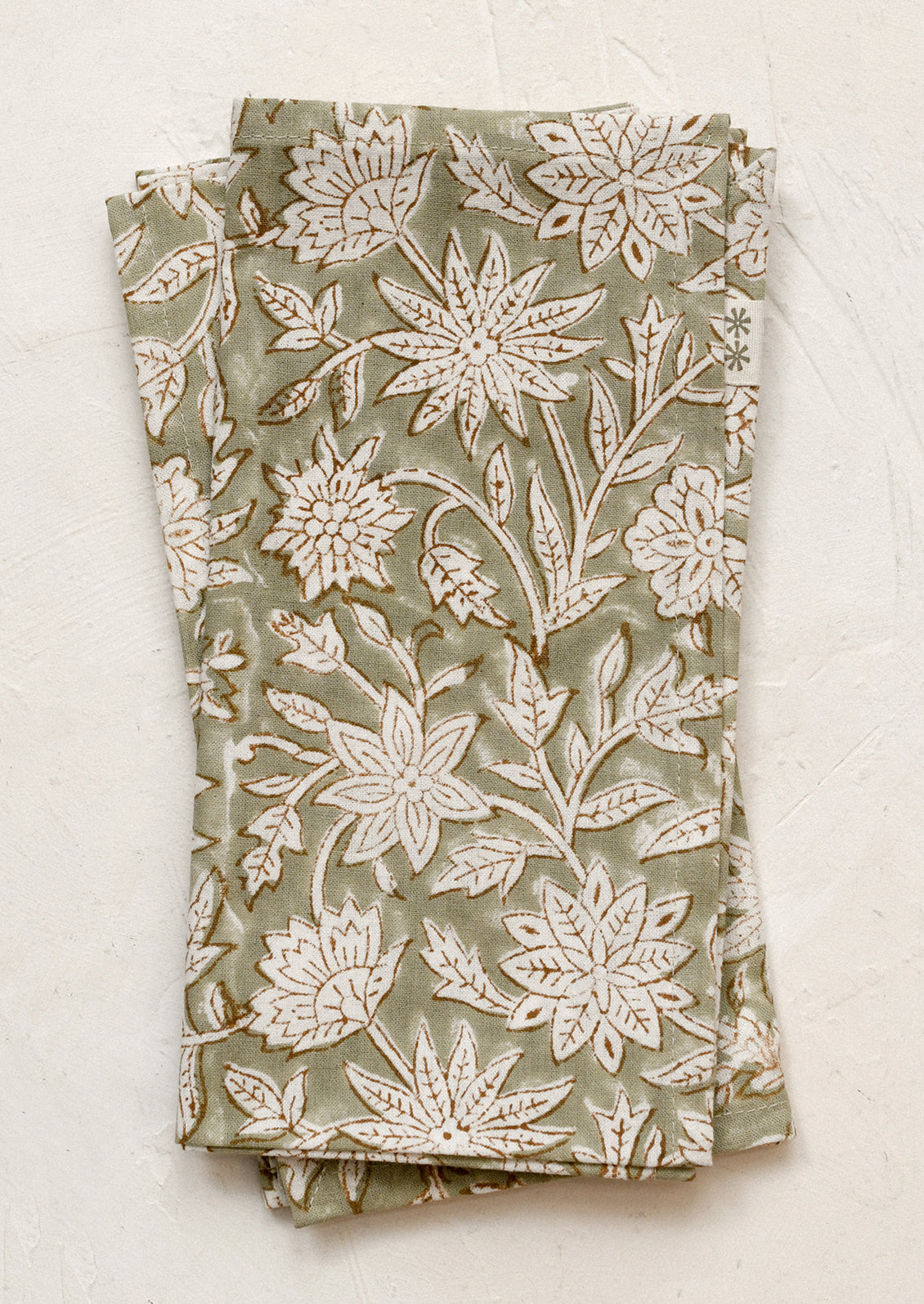 A pair of napkins in muted green color with white and brown block printed floral pattern.