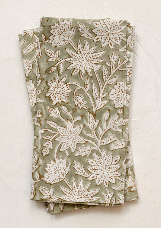 A pair of napkins in muted green color with white and brown block printed floral pattern.