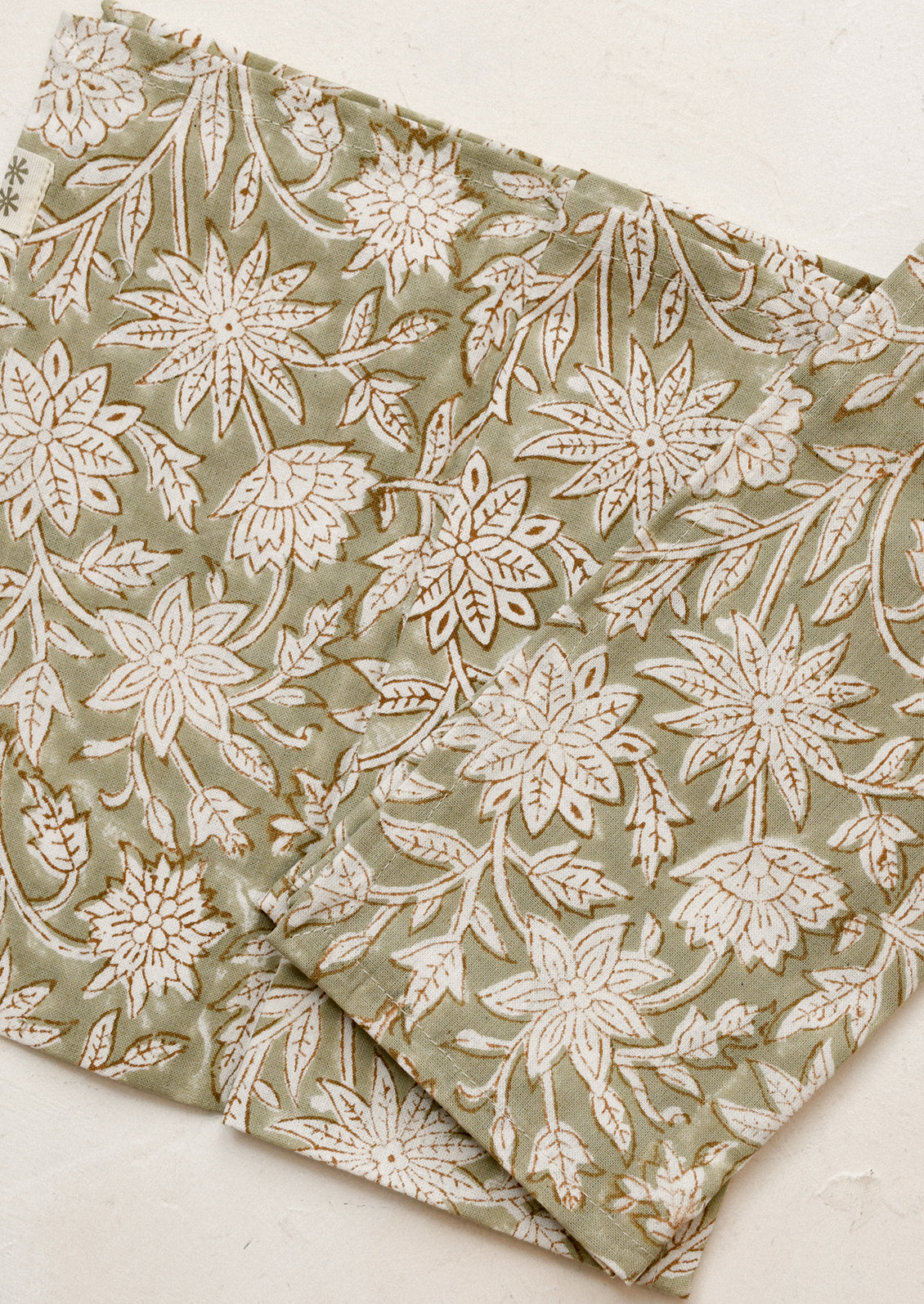 A pair of napkins in muted green color with white and brown block printed floral pattern.