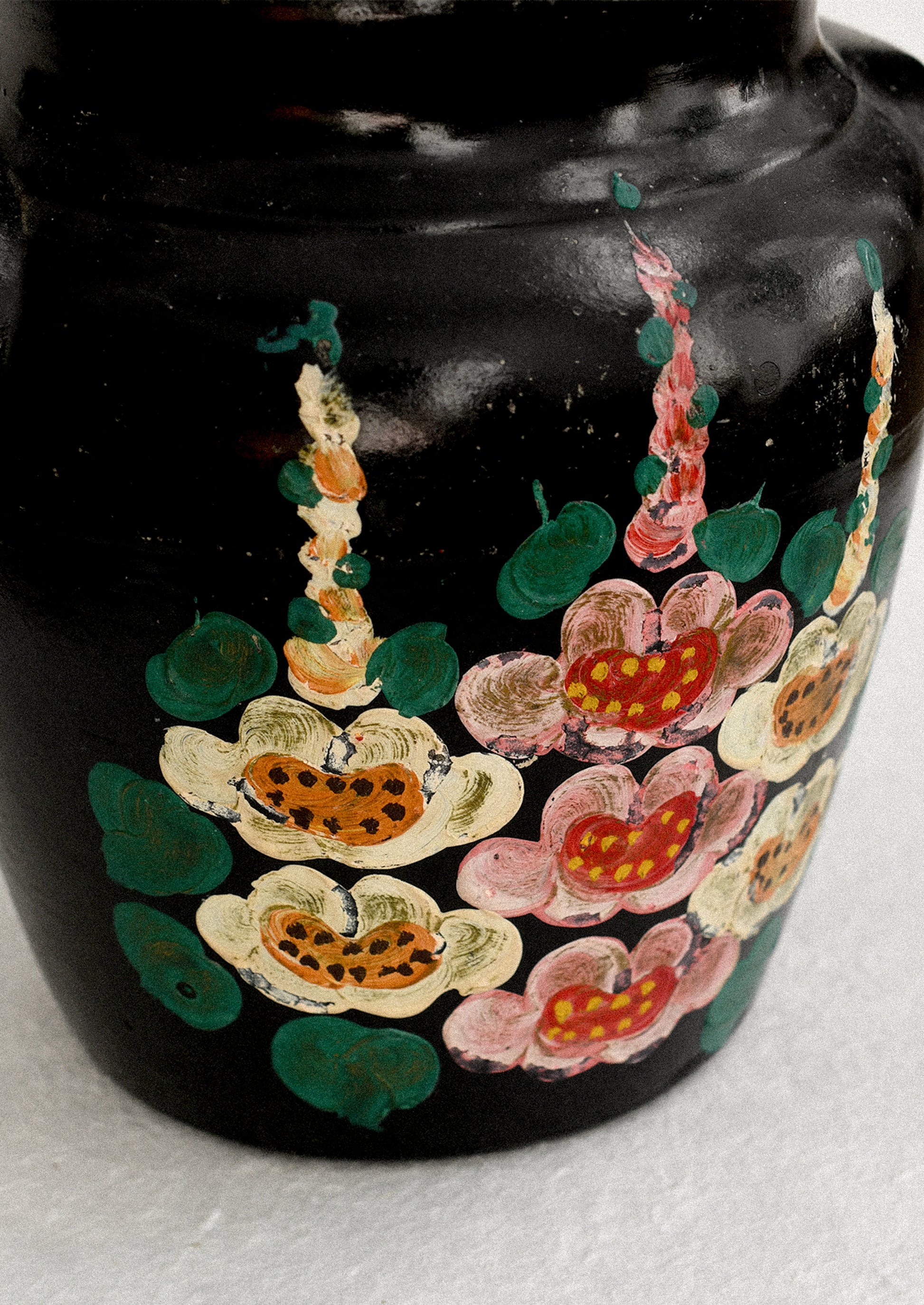 A vintage lidded crock in black with hand painted hollyhock pattern in pink and yellow.