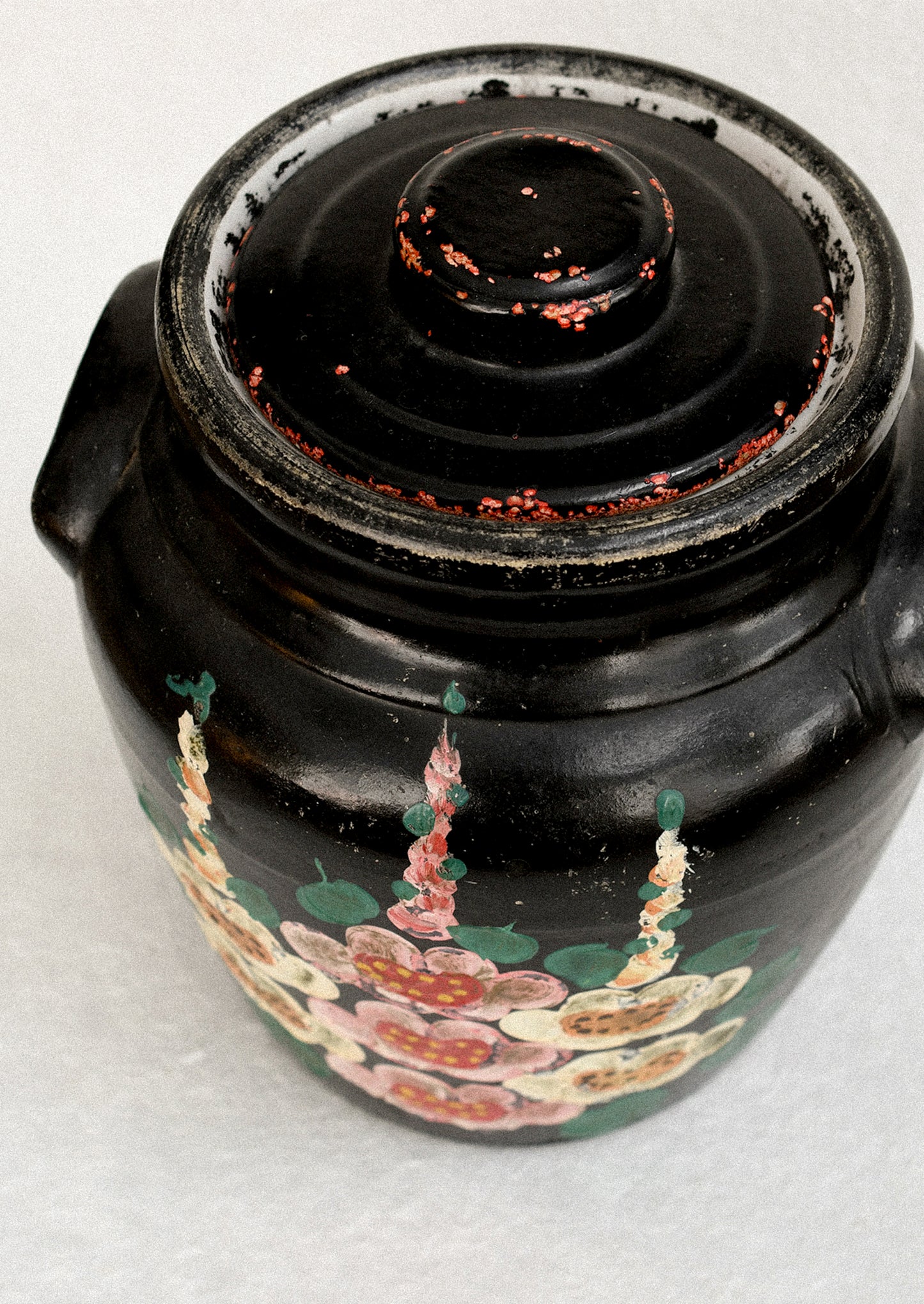 A vintage lidded crock in black with hand painted hollyhock pattern in pink and yellow.
