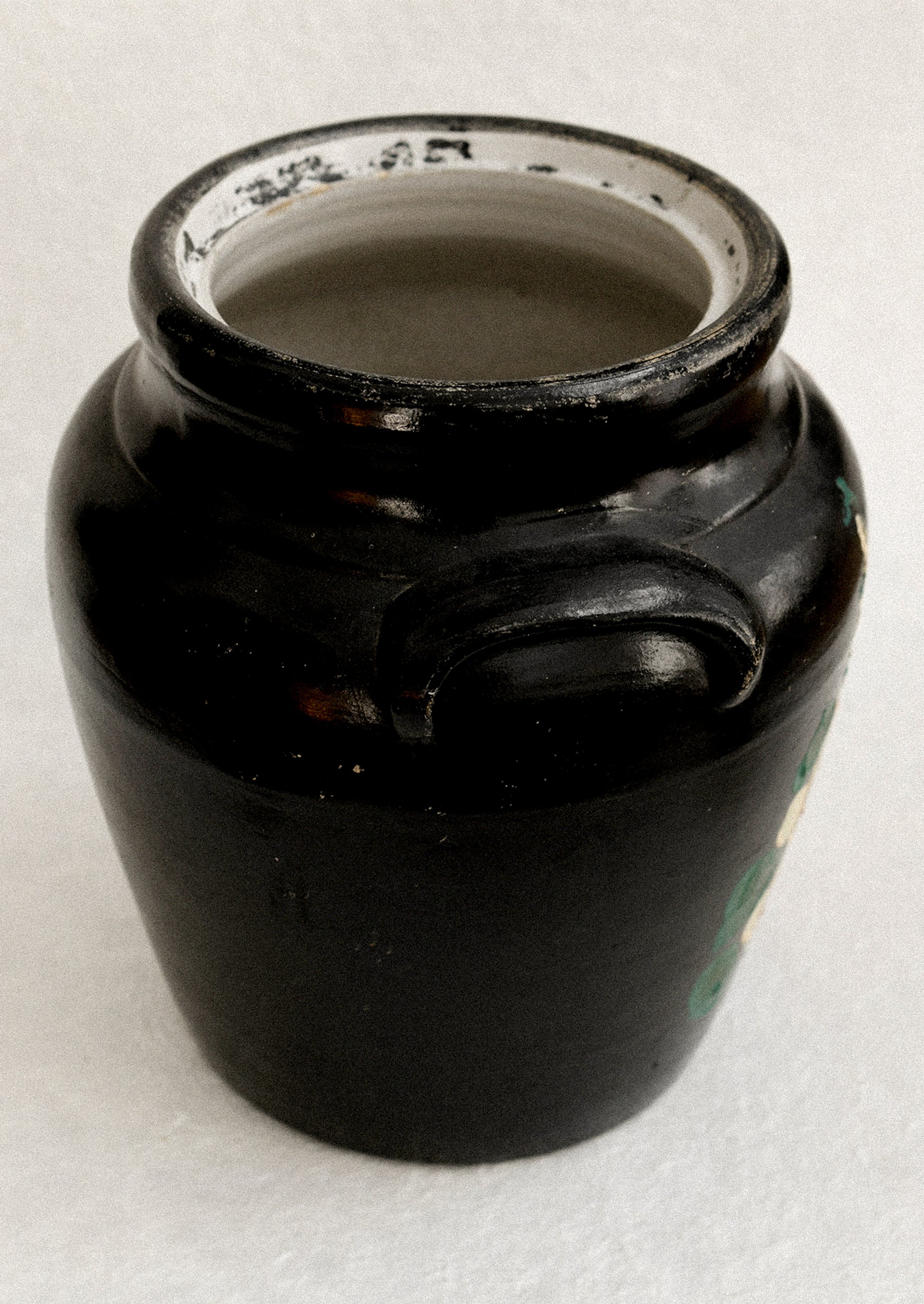 A vintage lidded crock in black with hand painted hollyhock pattern in pink and yellow.