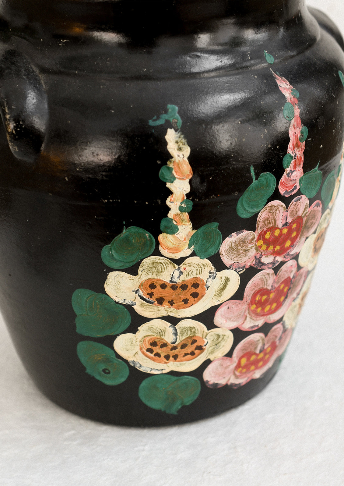 A vintage lidded crock in black with hand painted hollyhock pattern in pink and yellow.