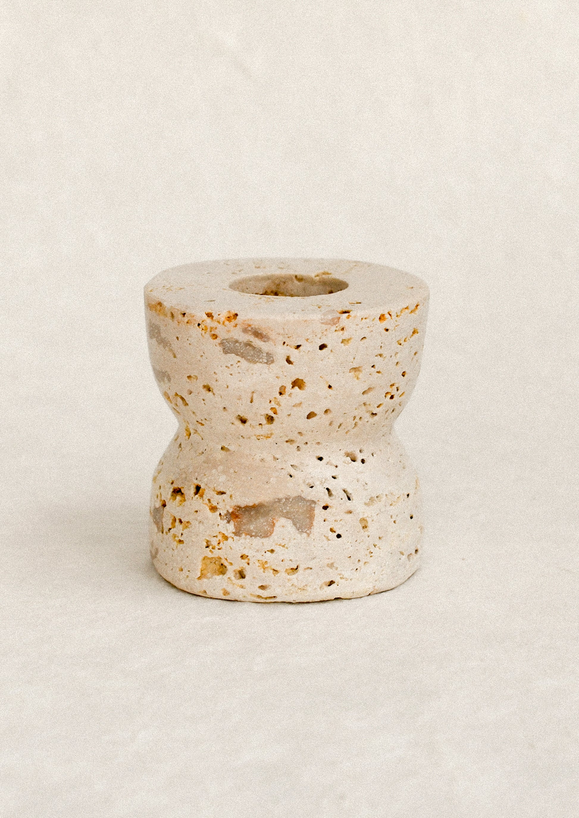 A natural travertine taper candle holder in short height.