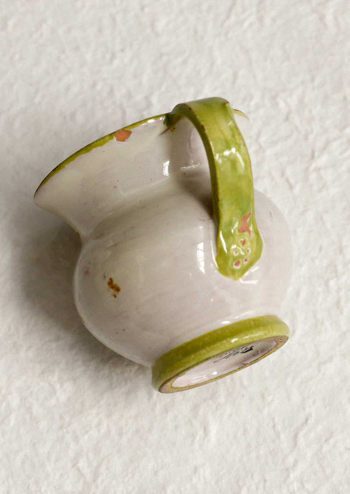 A small ceramic pitcher with painted floral design and green border.