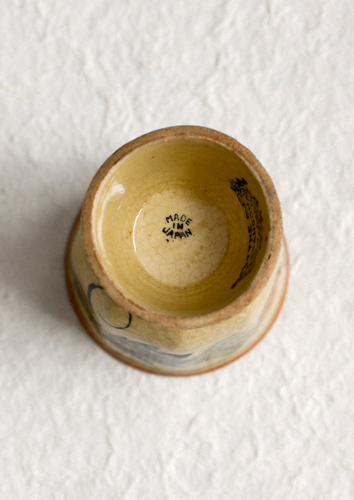 An antique egg cup in tan ceramic with caramel colored trim, and nasturtium floral pattern.