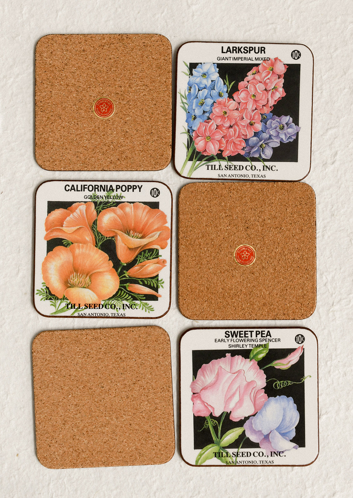 Set of six cork coasters with floral seed packet designs on a white background