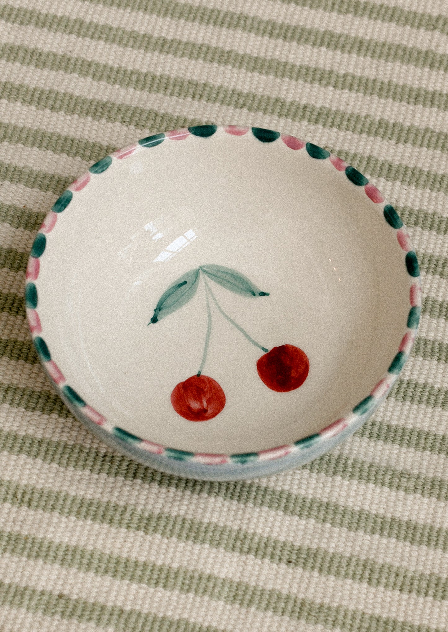 Small white ceramic bowl with cherry design on a striped fabric background.