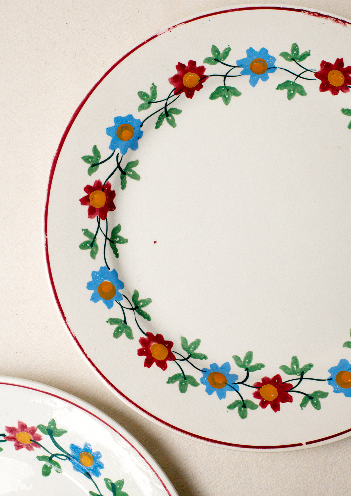 A pair of white plates with blue and red floral pattern around rim.